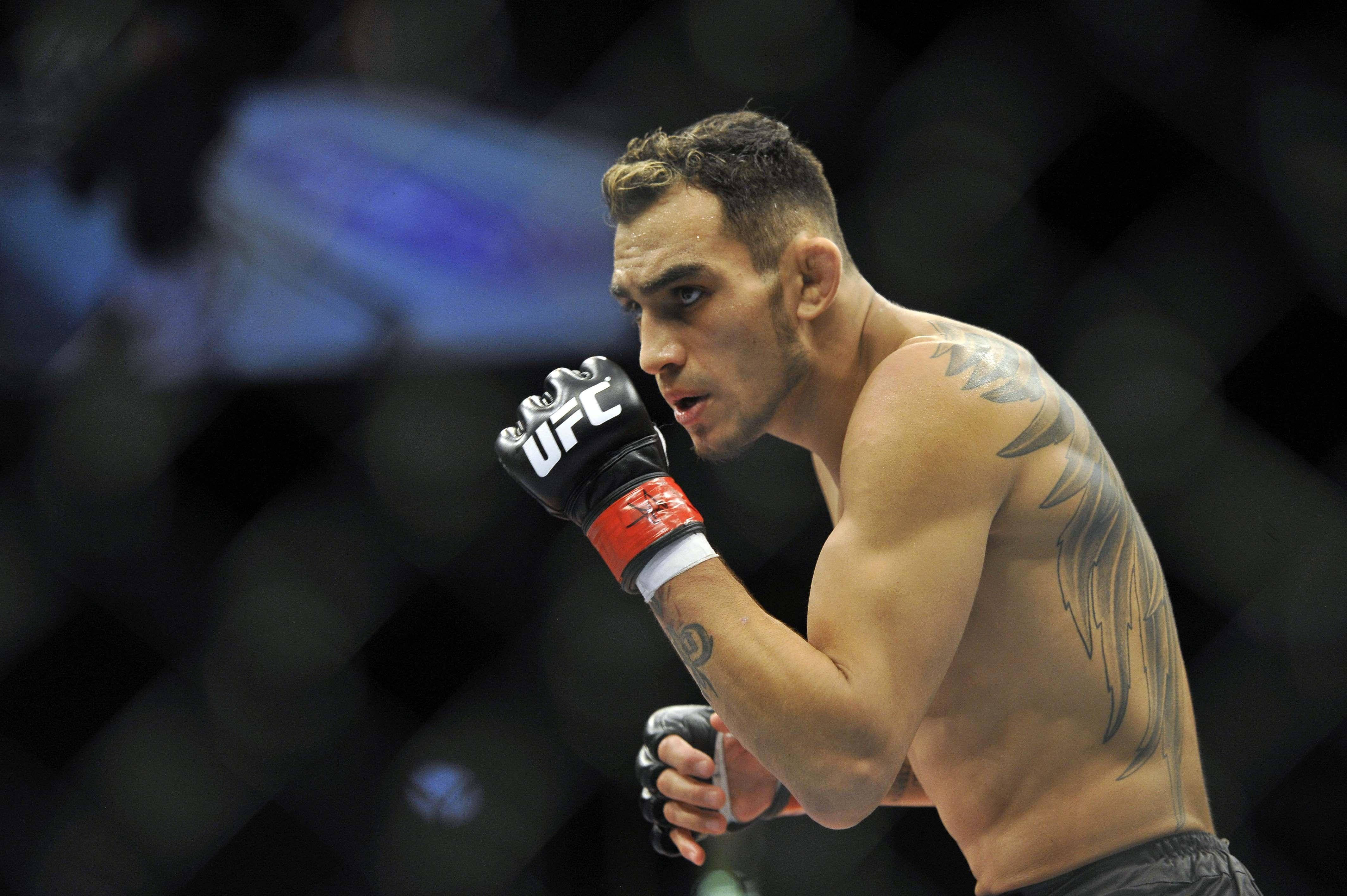 UFC 桌布 壁紙 — 一位專注的綜合格鬥選手戴著UFC手套，背上有刺青，眼神銳利，站在八角籠內準備就緒。