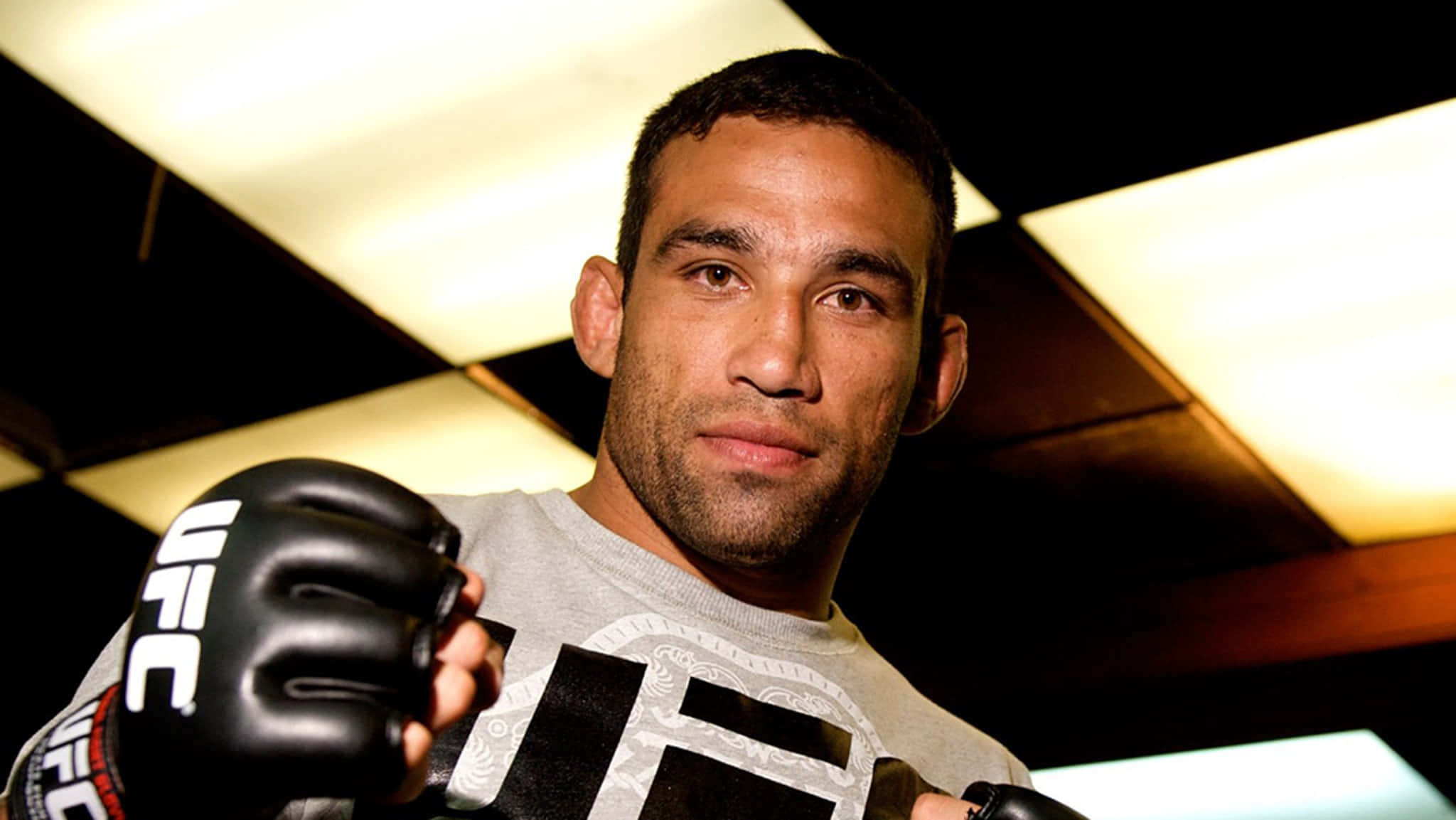 MMA 桌布 壁紙 — 一位專注的綜合格鬥選手戴著UFC手套，在幾何天花板燈光下凝視鏡頭。