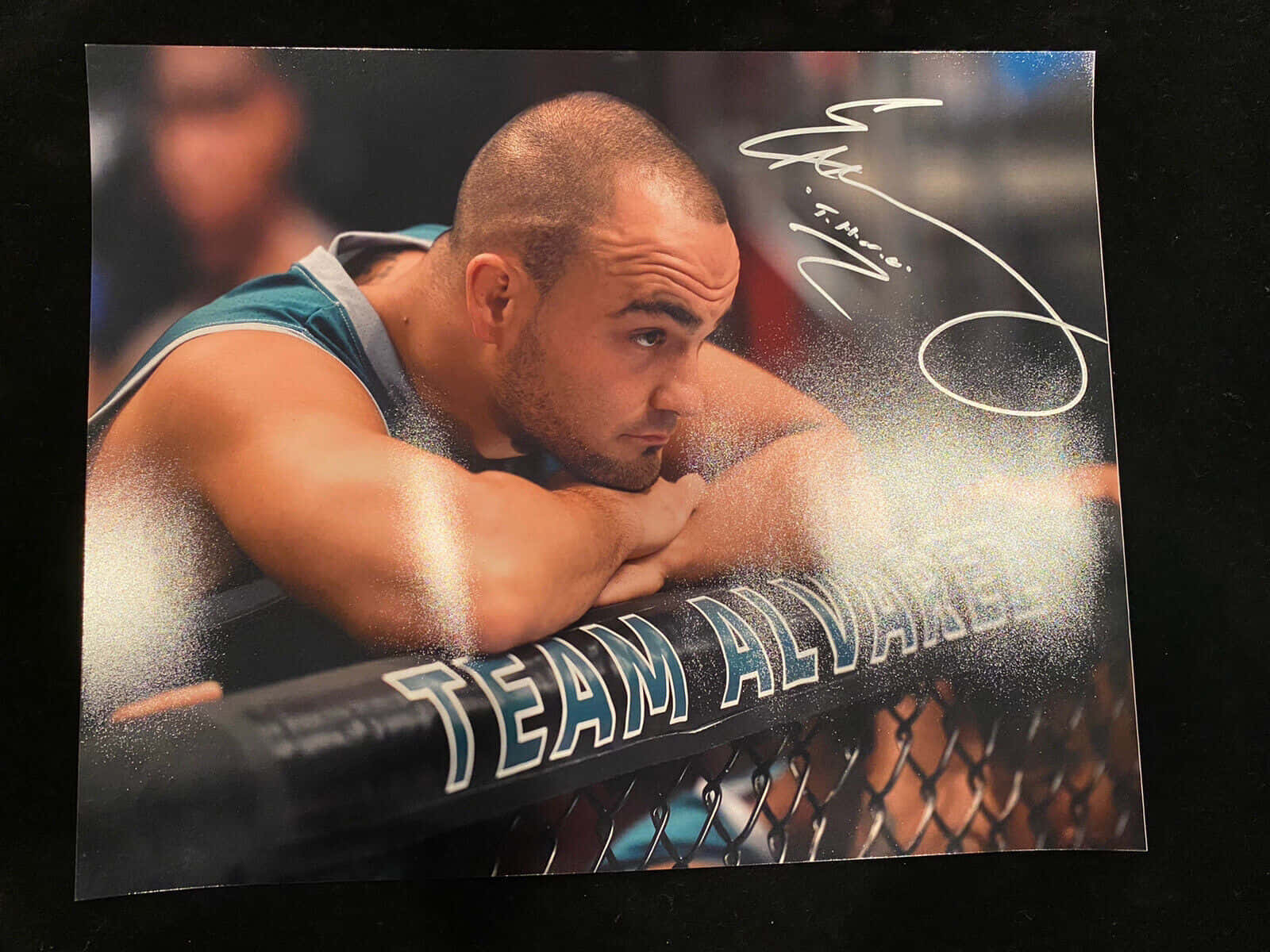 UFC 桌布 壁紙 — 一位專注的綜合格鬥選手靠在印有「TEAM ALVAREZ」標誌的籠網上，白色粉末在他周圍爆炸。
