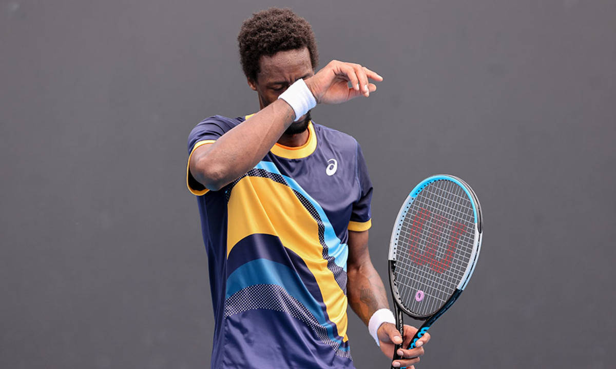 Tennis 桌布 壁紙 — 一位專注的網球運動員在純灰色背景下拿著 Wilson 球拍擦去額頭上的汗水。