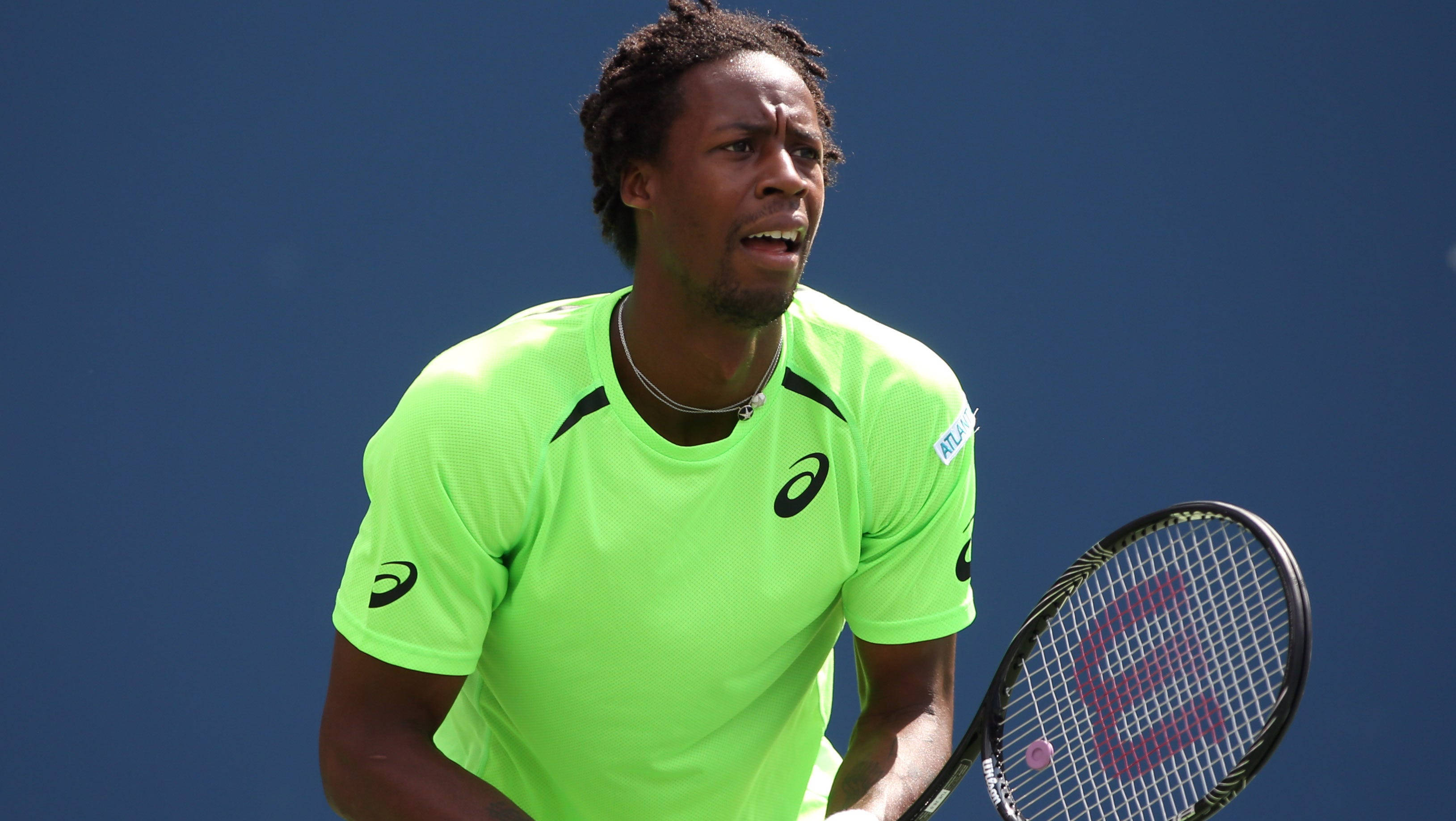 Tennis 桌布 壁紙 — 一位專注的網球運動員穿著螢光綠色襯衫，在明亮的日光下，在純藍色背景前緊握球拍。