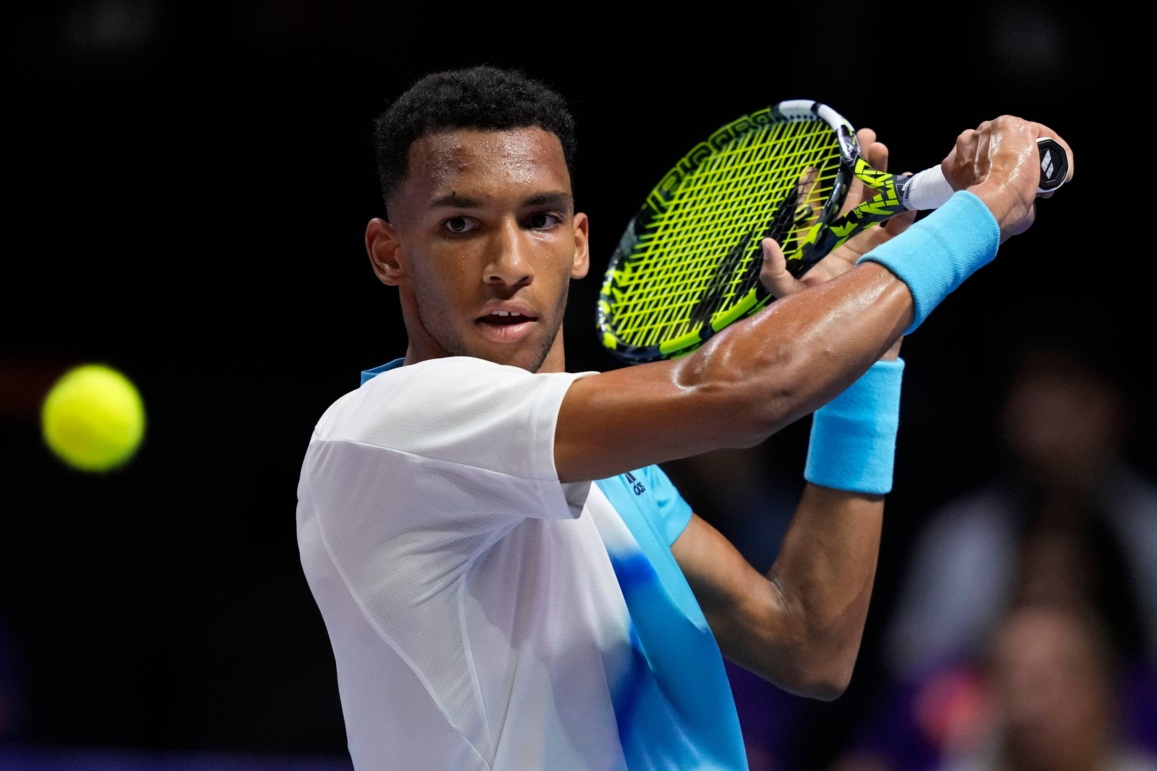 felix auger aliassime 桌布 壁紙 — 一位專注的網球選手在場館燈光下揮動亮黃色球拍擊球。