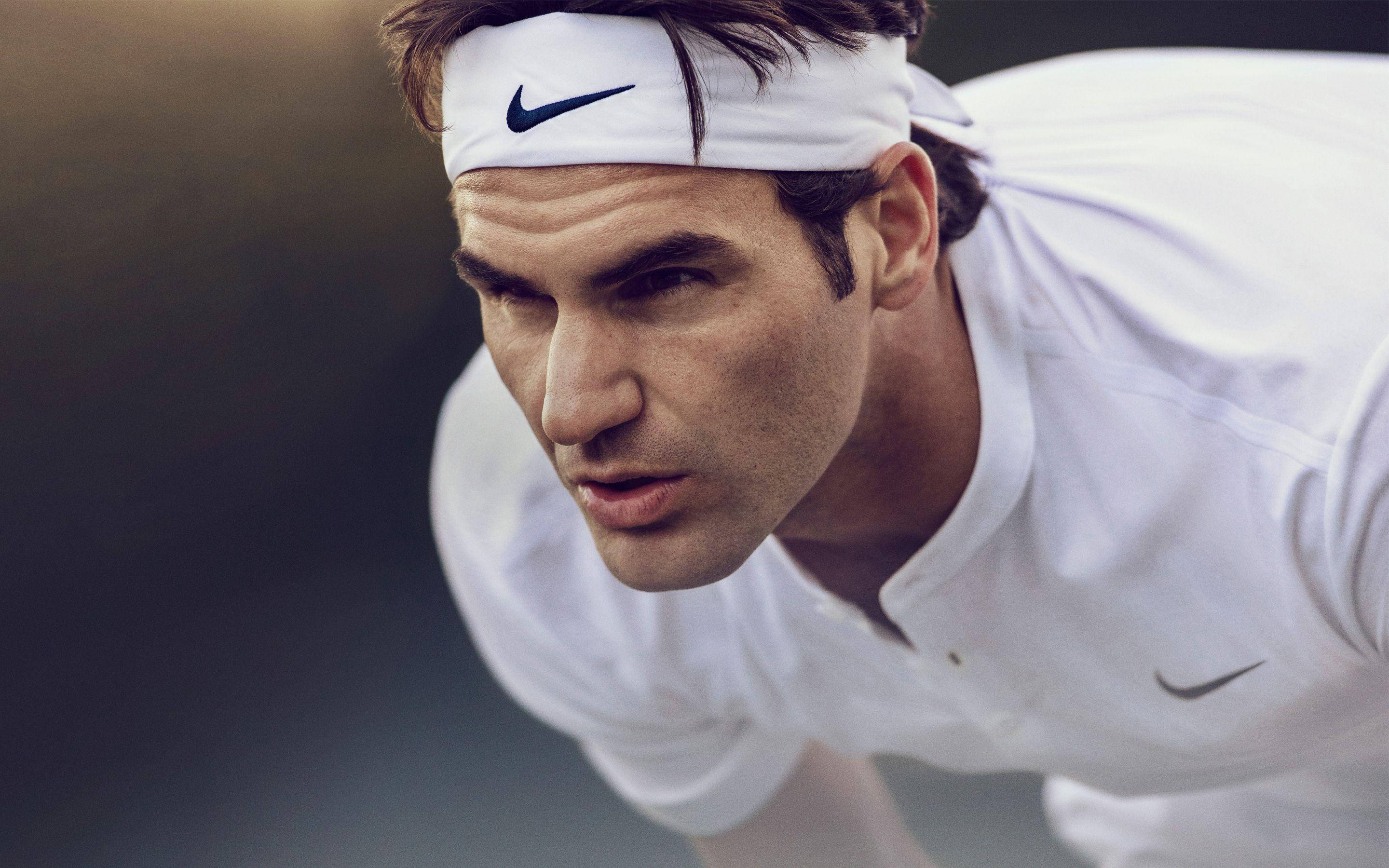 roger 桌布 壁紙 — 一位專注的網球選手身穿白色Nike裝備，在比賽中帶著強烈的決心向前傾。