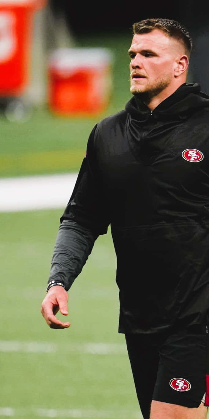 Mike Mcglinchey 桌布 壁紙 — 一位專注的美式足球員身穿黑色舊金山四九人裝備，站在綠色球場上，球場燈光照射。