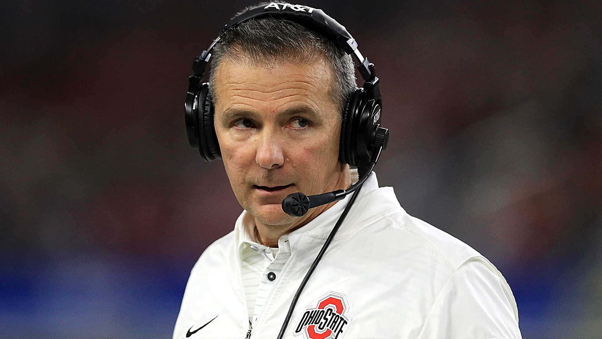 Urban Meyer 桌布 壁紙 — 一位專注的美式足球教練在比賽期間戴著耳機和白色俄亥俄州立大學外套在邊線。