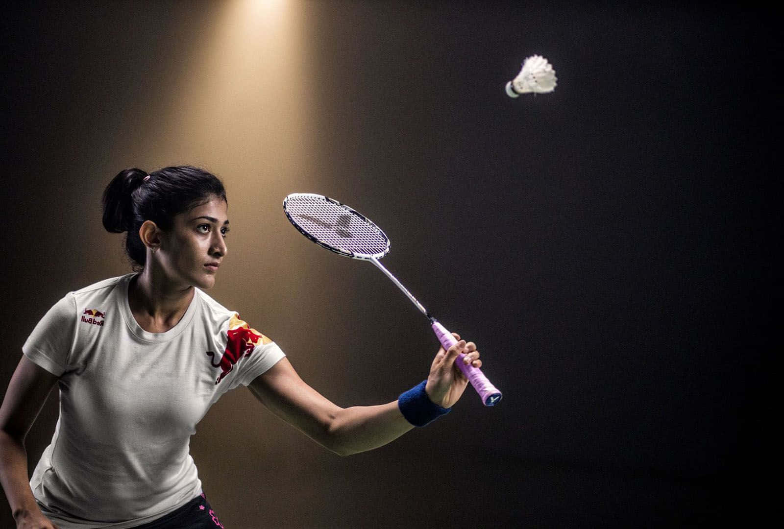 Best Badminton 桌布 壁紙 — 一位專注的羽球運動員在聚光燈下揮拍擊球，背景昏暗。
