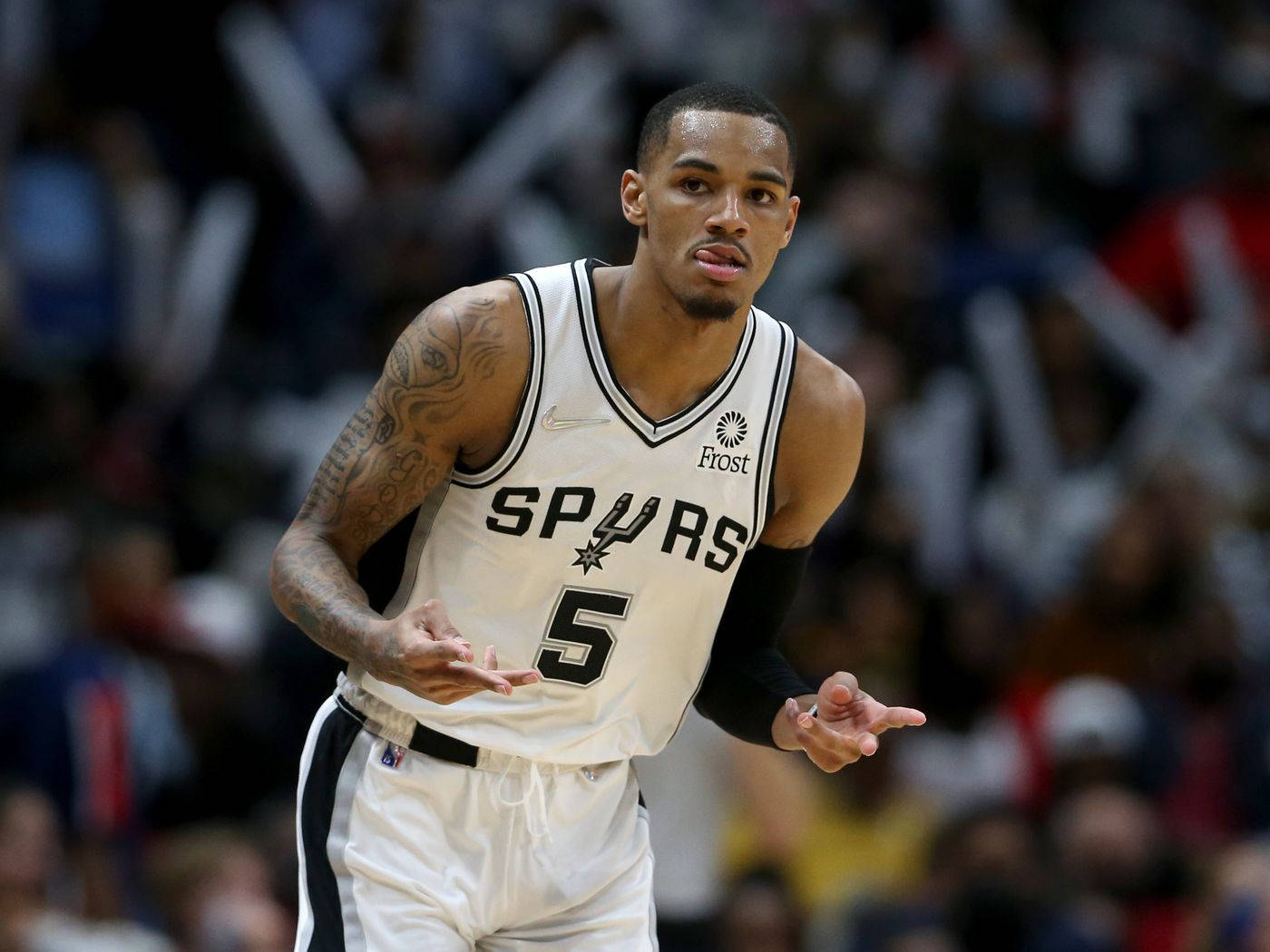 Dejounte Murray 桌布 壁紙 — 一位專注的聖安東尼奧馬刺籃球運動員，身穿白色5號球衣，在模糊的人群背景下比賽中做手勢。