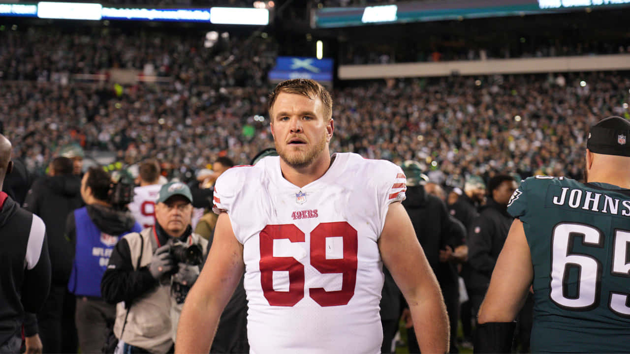 Mike Mcglinchey 桌布 壁紙 — 一位專注的舊金山四九人美式足球員身穿白色69號球衣，在比賽期間站在球場上，身後是座無虛席的體育場。