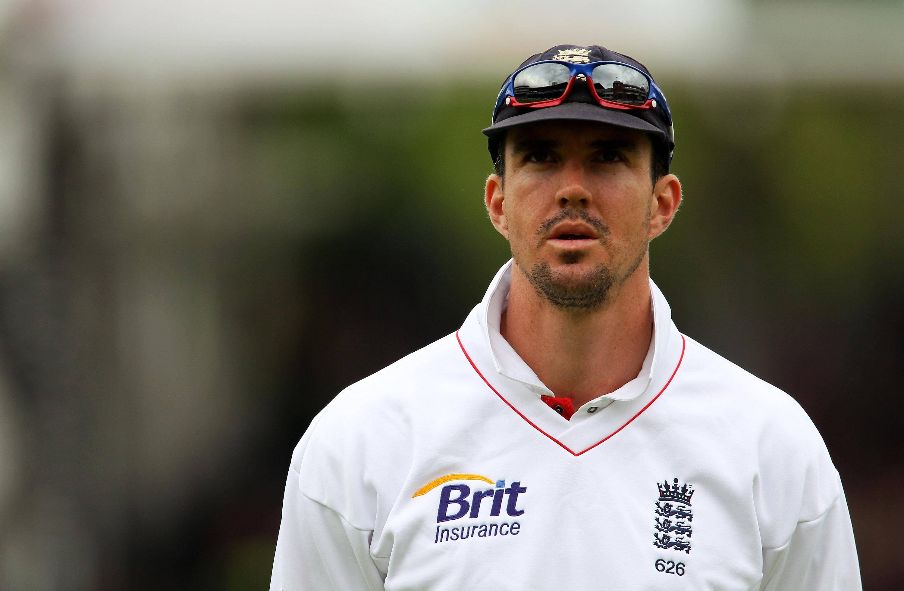 England Cricket 桌布 壁紙 — 一位專注的英格蘭板球運動員，身穿白色制服和帽子，帽上架著太陽眼鏡，專注地向前凝視。