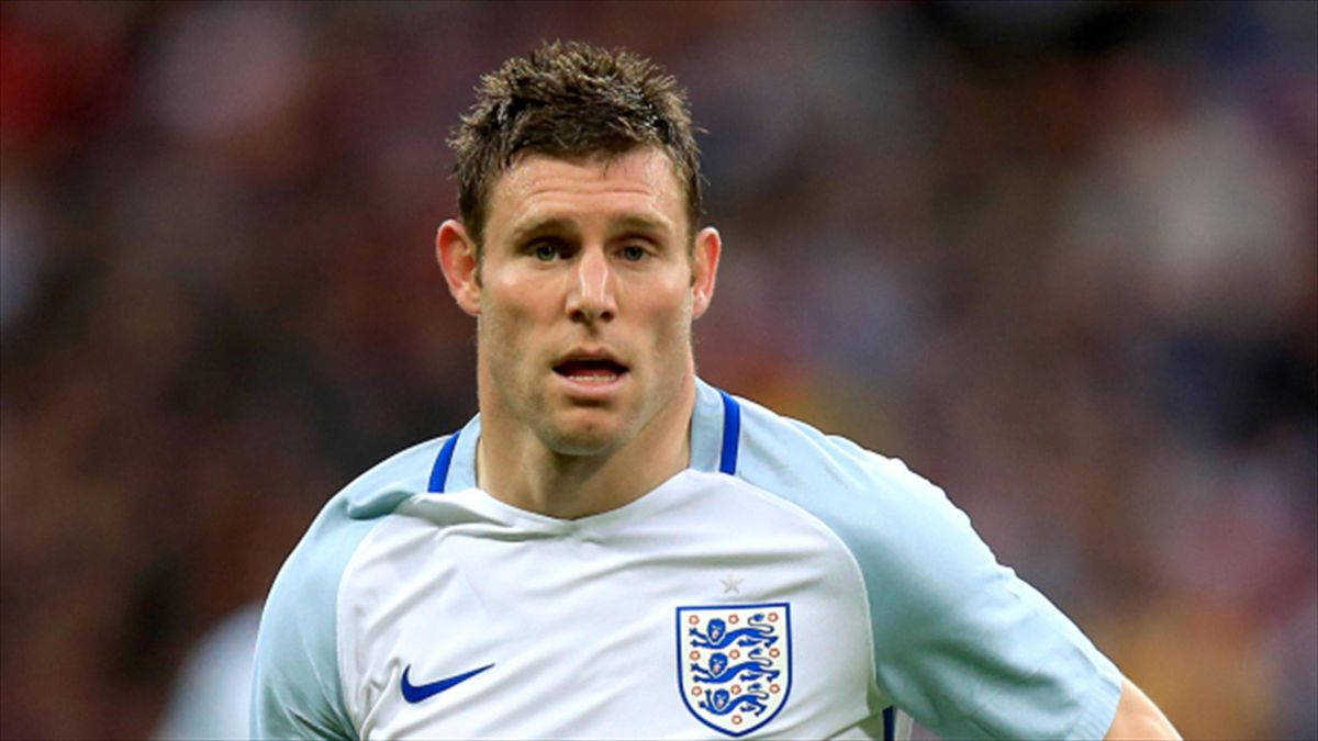 Football Players 桌布 壁紙 — 一位專注的英格蘭足球員，身穿淺藍色和白色球衣，帶有三獅標誌，在比賽中專注地向前看。