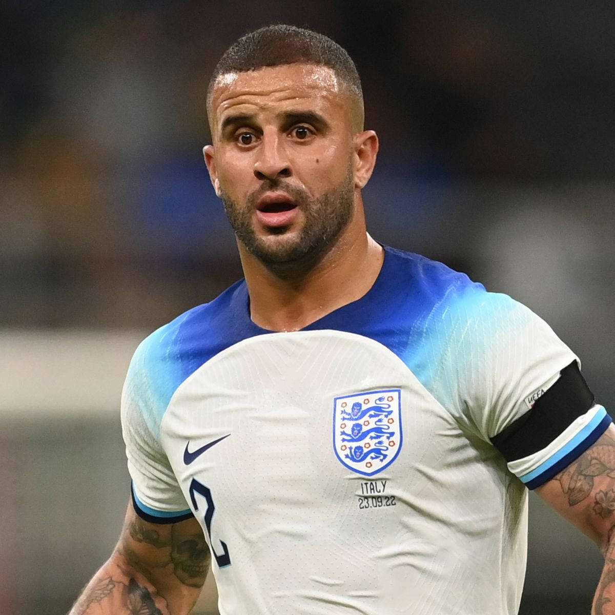 Kyle Walker 桌布 壁紙 — 一位專注的英格蘭足球員，身穿白色和藍色球衣，比賽期間手臂上可見刺青。