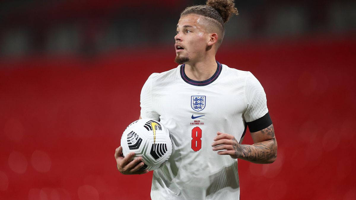 Football Players 桌布 壁紙 — 一位專注的英格蘭足球員身穿白色球衣，在模糊的紅色球場背景下抱著足球。
