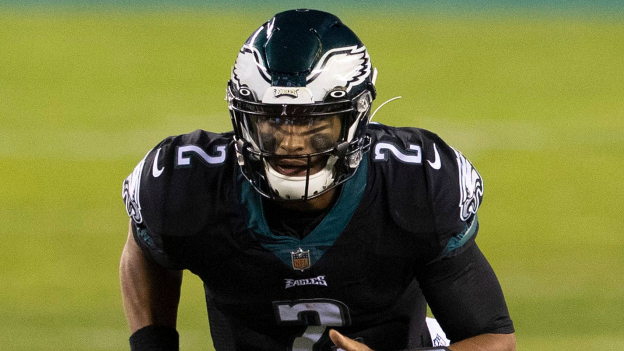 Jalen Hurts Eagles 桌布 壁紙 — 一位專注的費城老鷹隊四分衛穿著黑色和青綠色的球衣，在比賽期間蹲在綠色球場上。