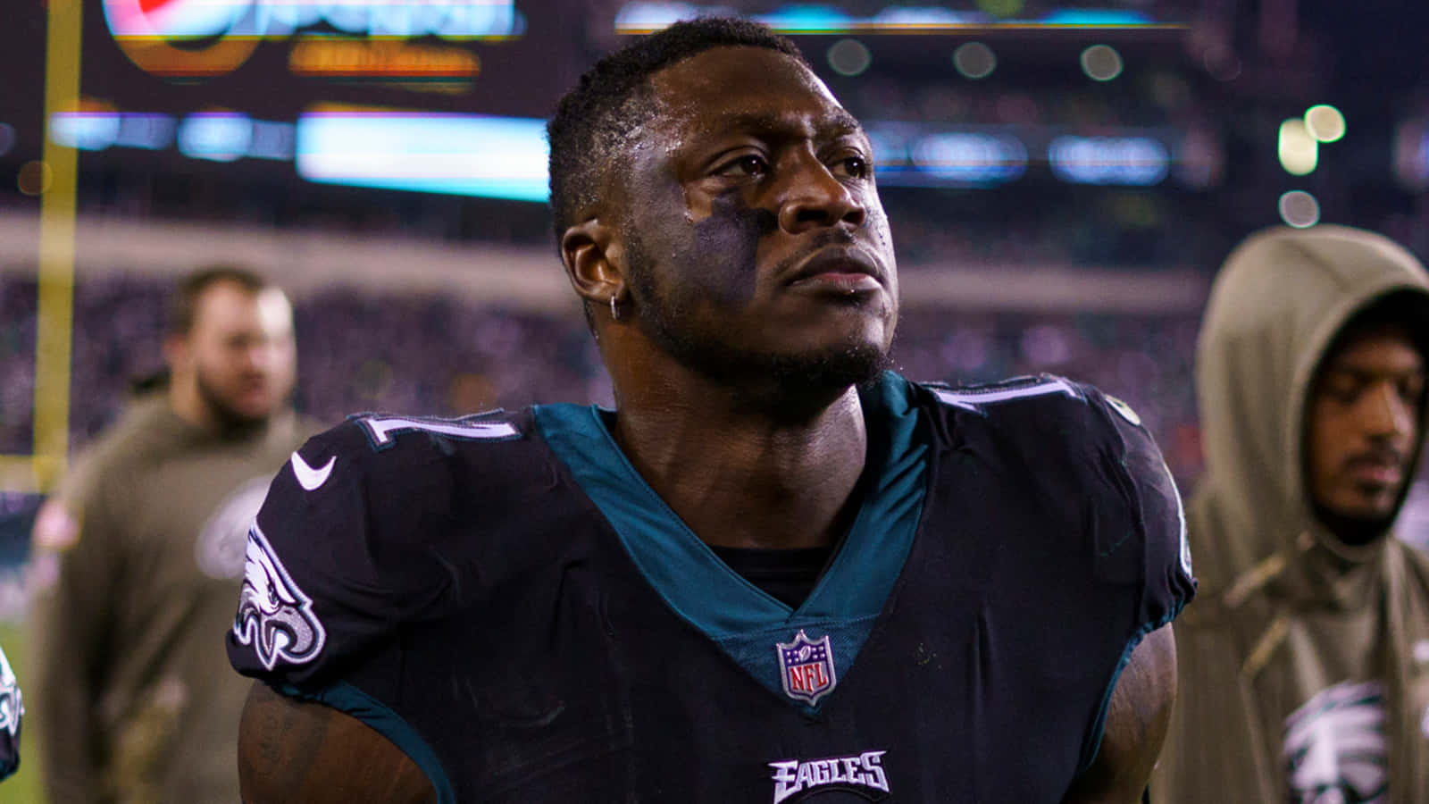 NFL 美式足球 桌布 壁紙 — 一位專注的費城老鷹隊美式足球員，臉上塗有顏料，在夜間比賽中於球場燈光下向上凝視。