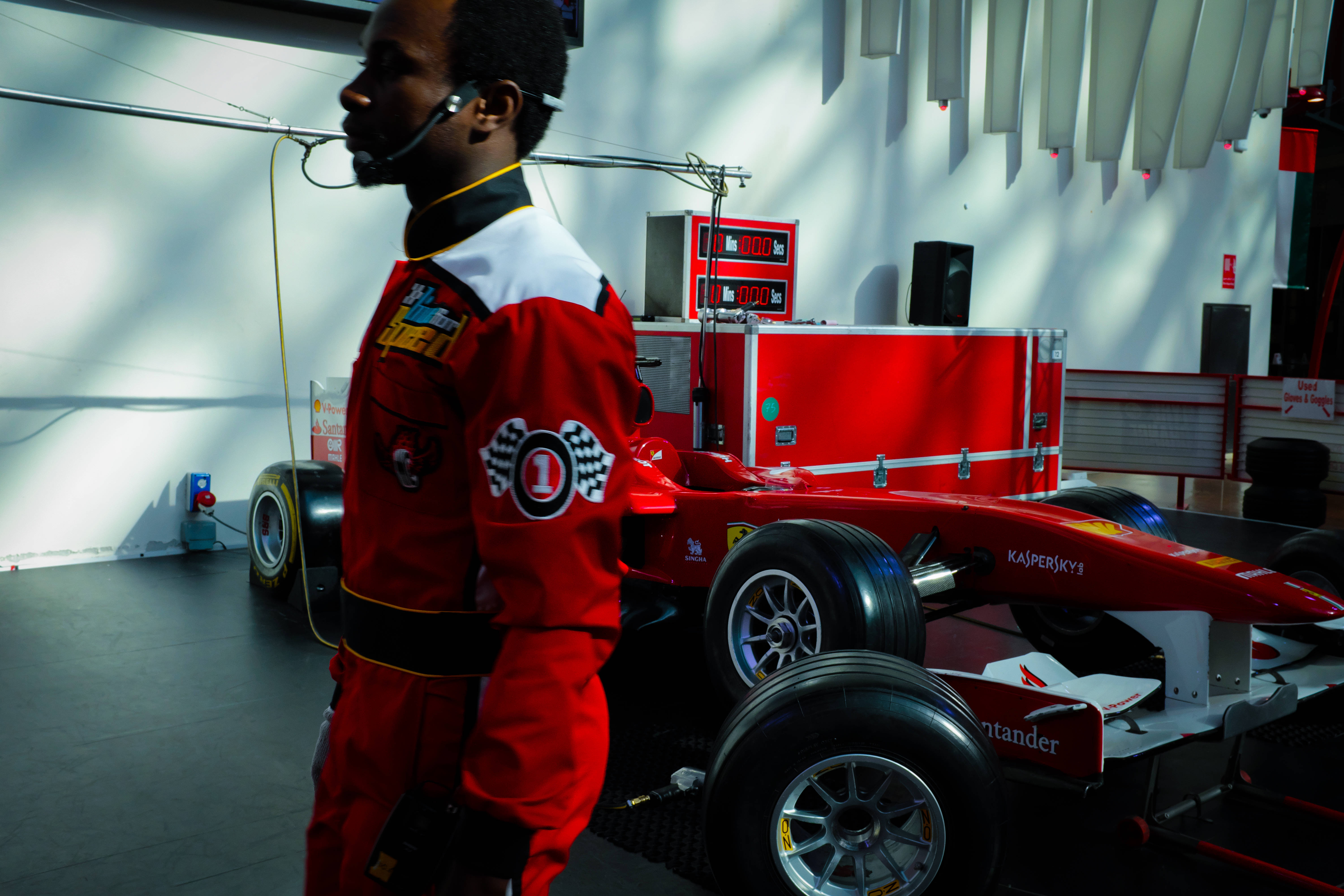 Racing 桌布 壁紙 — 一位專注的賽車手身穿紅色賽車服，站在明亮的車庫中一輛流線型紅色一級方程式賽車旁。