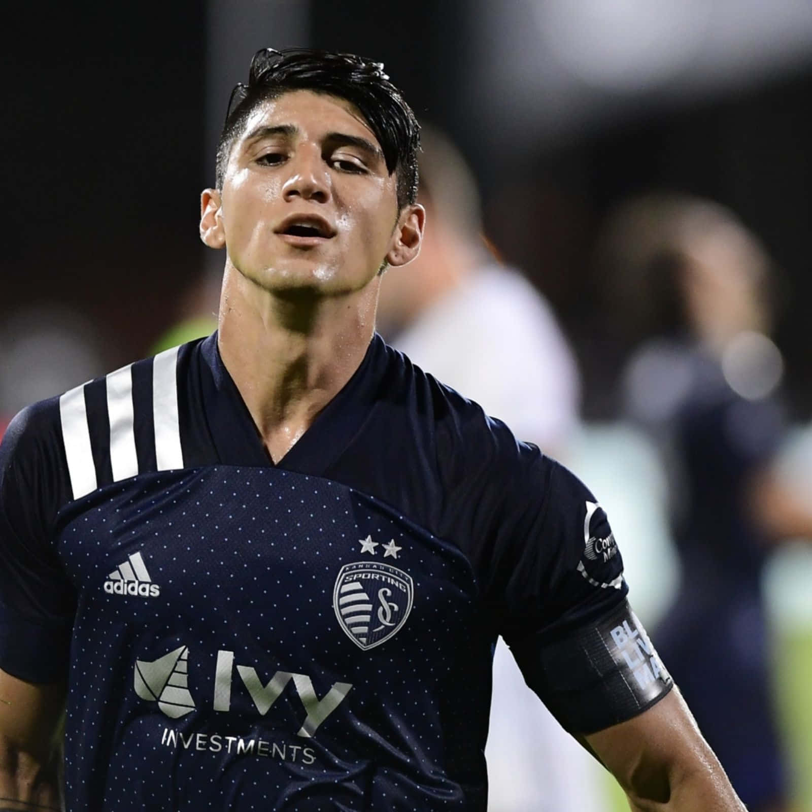足球 桌布 壁紙 — 一位專注的足球員身穿深藍色Sporting Kansas City球衣，在夜間比賽中決心向上看。