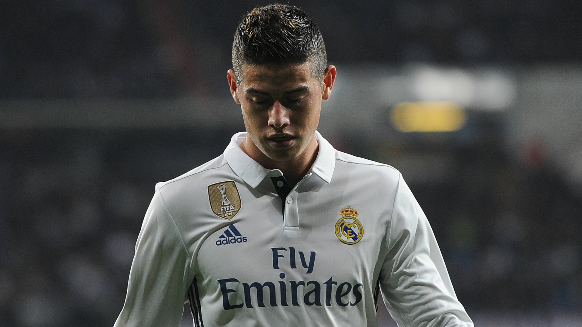 James Rodriguez 桌布 壁紙 — 一位專注的足球員身穿白色皇家馬德里球衣，在夜間比賽中堅定地低頭。