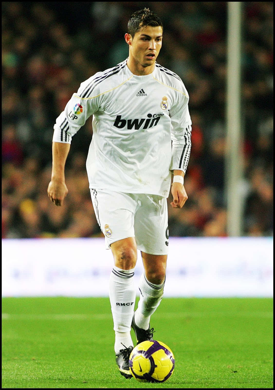 Ronaldo 桌布 壁紙 — 一位專注的足球員身穿白色皇家馬德里球衣，在球場燈光下於綠色草地上控制一個黃色和紫色的球。