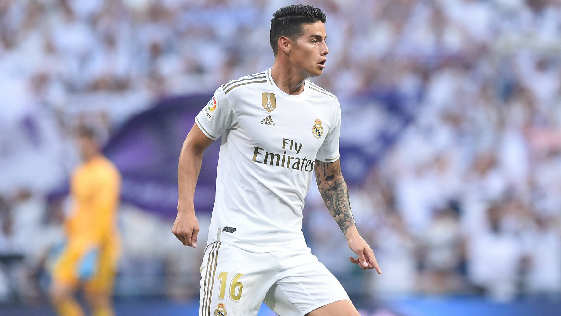 James Rodriguez 桌布 壁紙 — 一位專注的足球員身穿白色皇家馬德里球衣，在陽光明媚的球場上奔跑，背景是模糊的體育場人群。