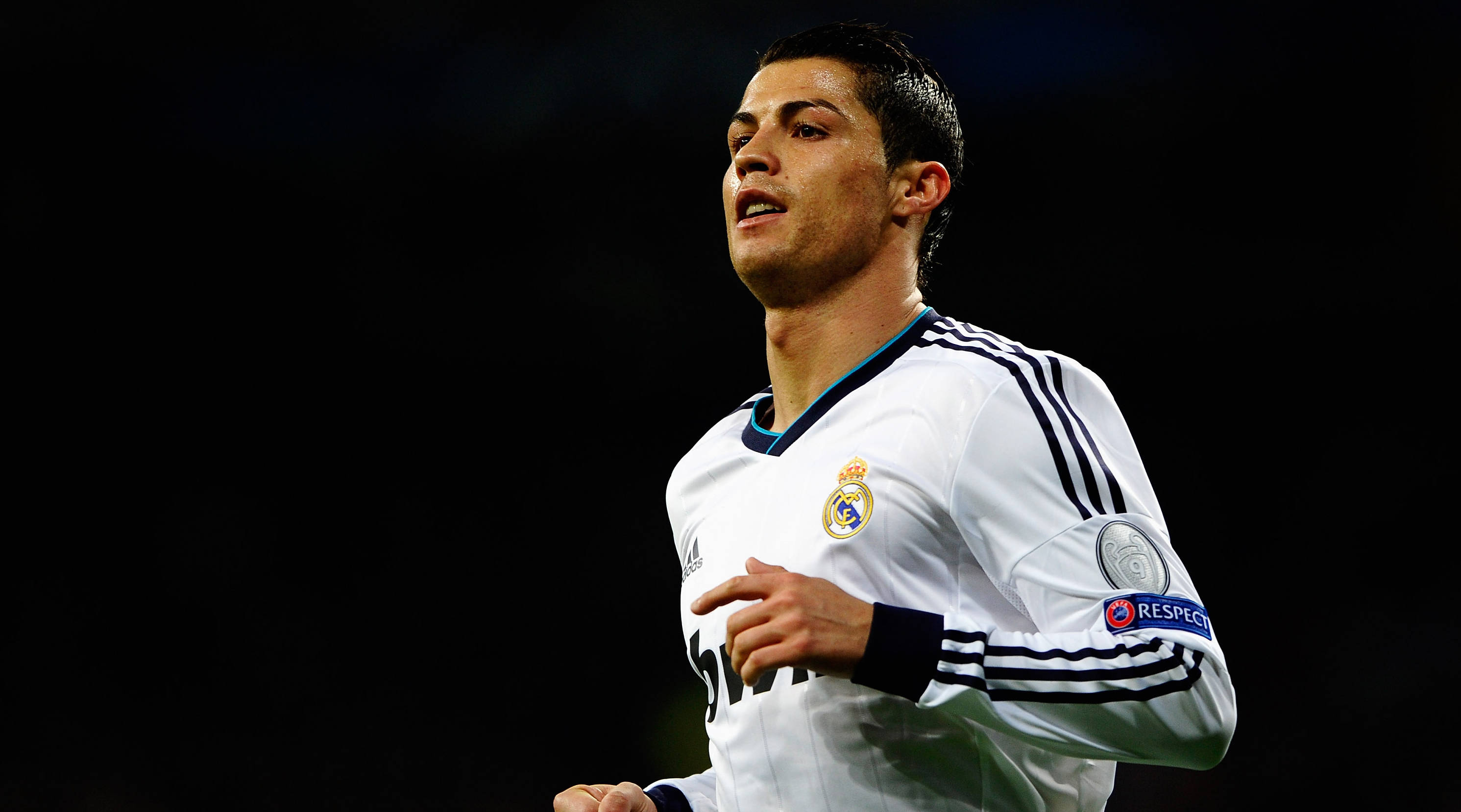 Cr7 桌布 壁紙 — 一位專注的足球員身穿白色皇家馬德里球衣，在球場燈光下以黑暗背景奔跑。
