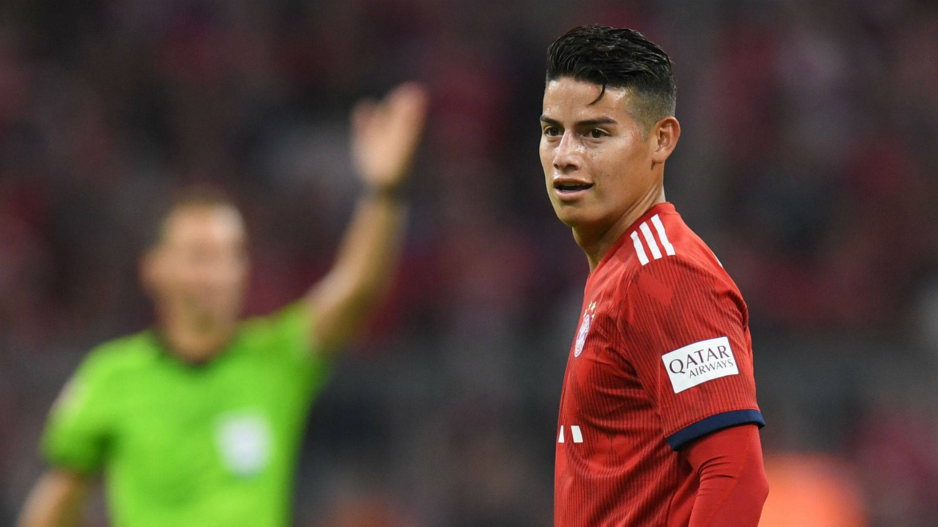 James Rodriguez 桌布 壁紙 — 一位專注的足球員身穿紅色球衣向球迷揮手，身後一位綠色裁判做著手勢。