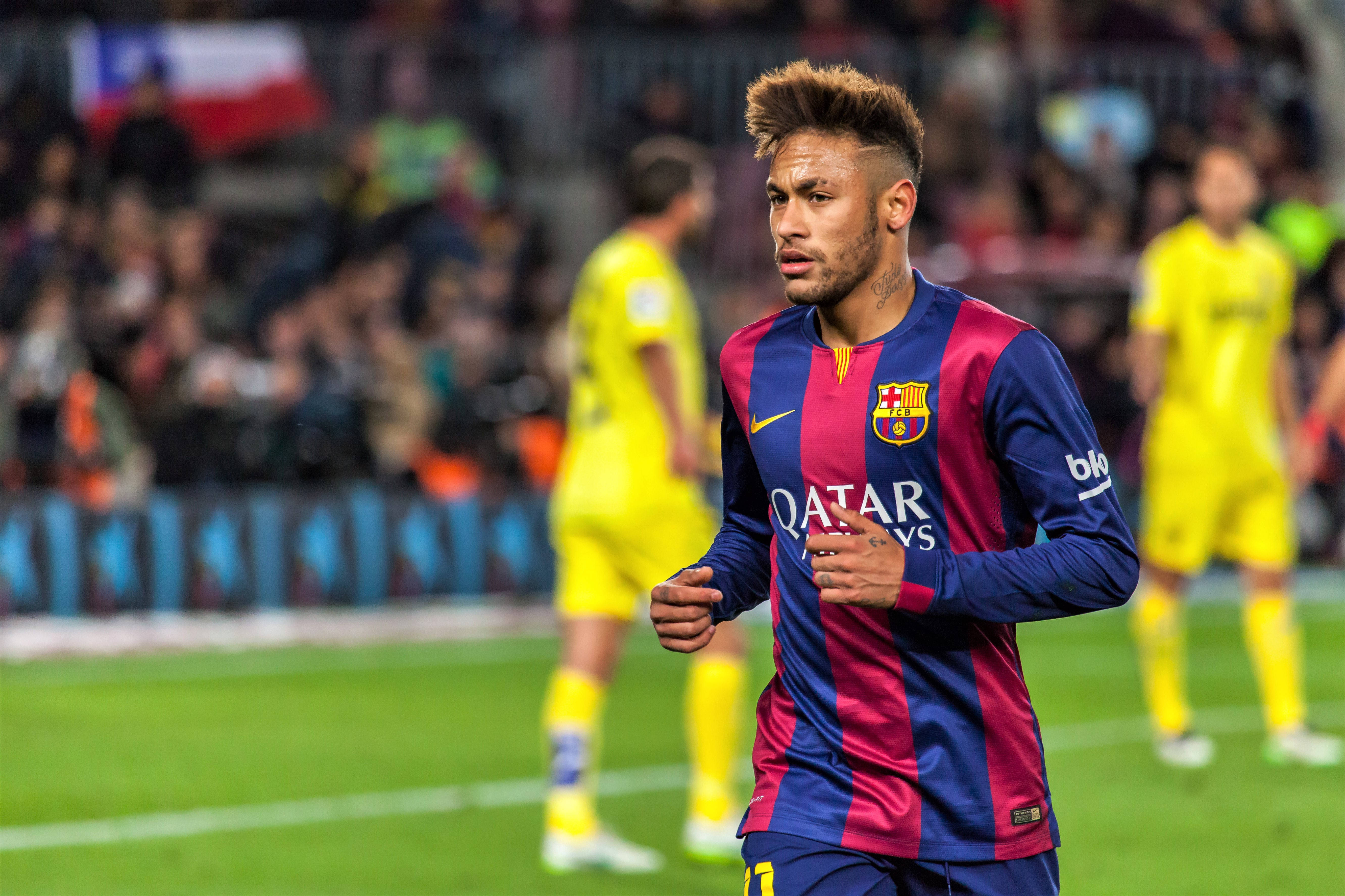 足球 桌布 壁紙 — 一位專注的足球員身穿藍紅條紋球衣，在球場燈光下站在充滿活力的綠色草地上。