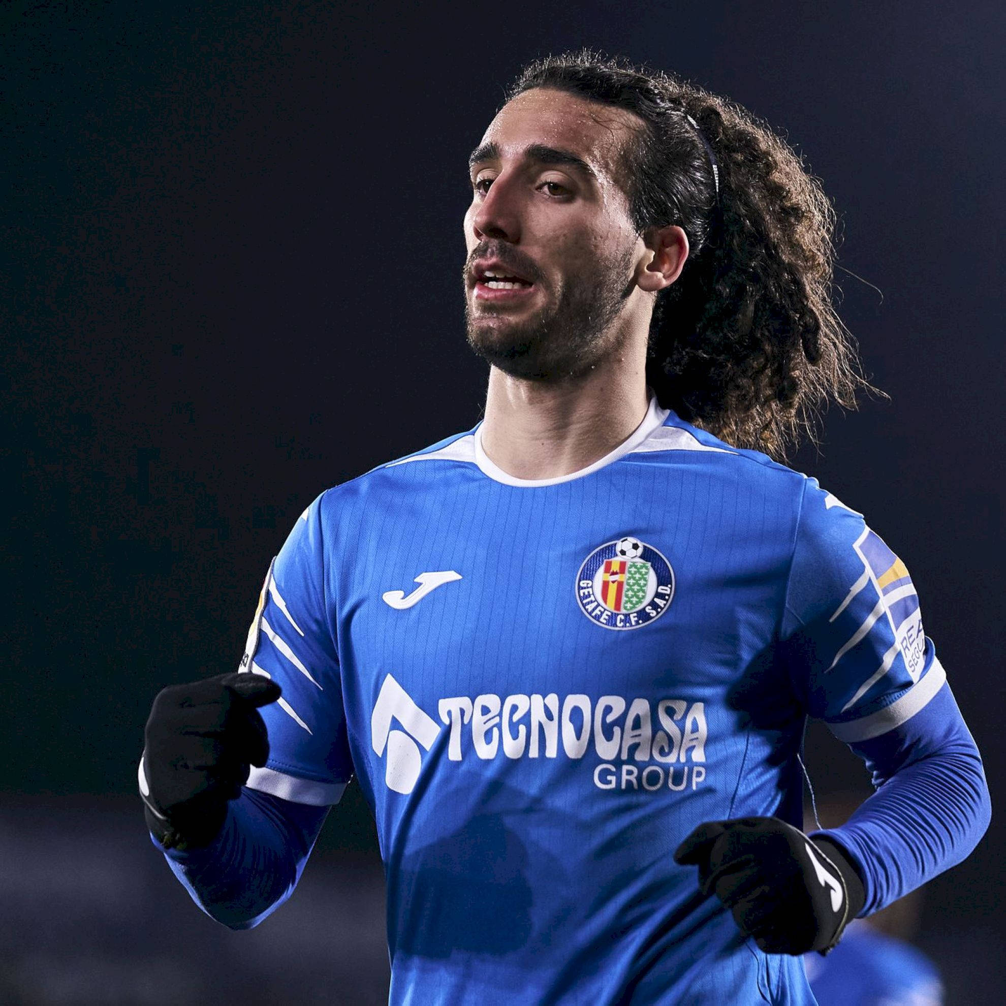 Football Players 桌布 壁紙 — 一位專注的足球員身穿藍色本菲卡球衣，在球場燈光下奔跑，留著捲髮並戴著黑色手套。