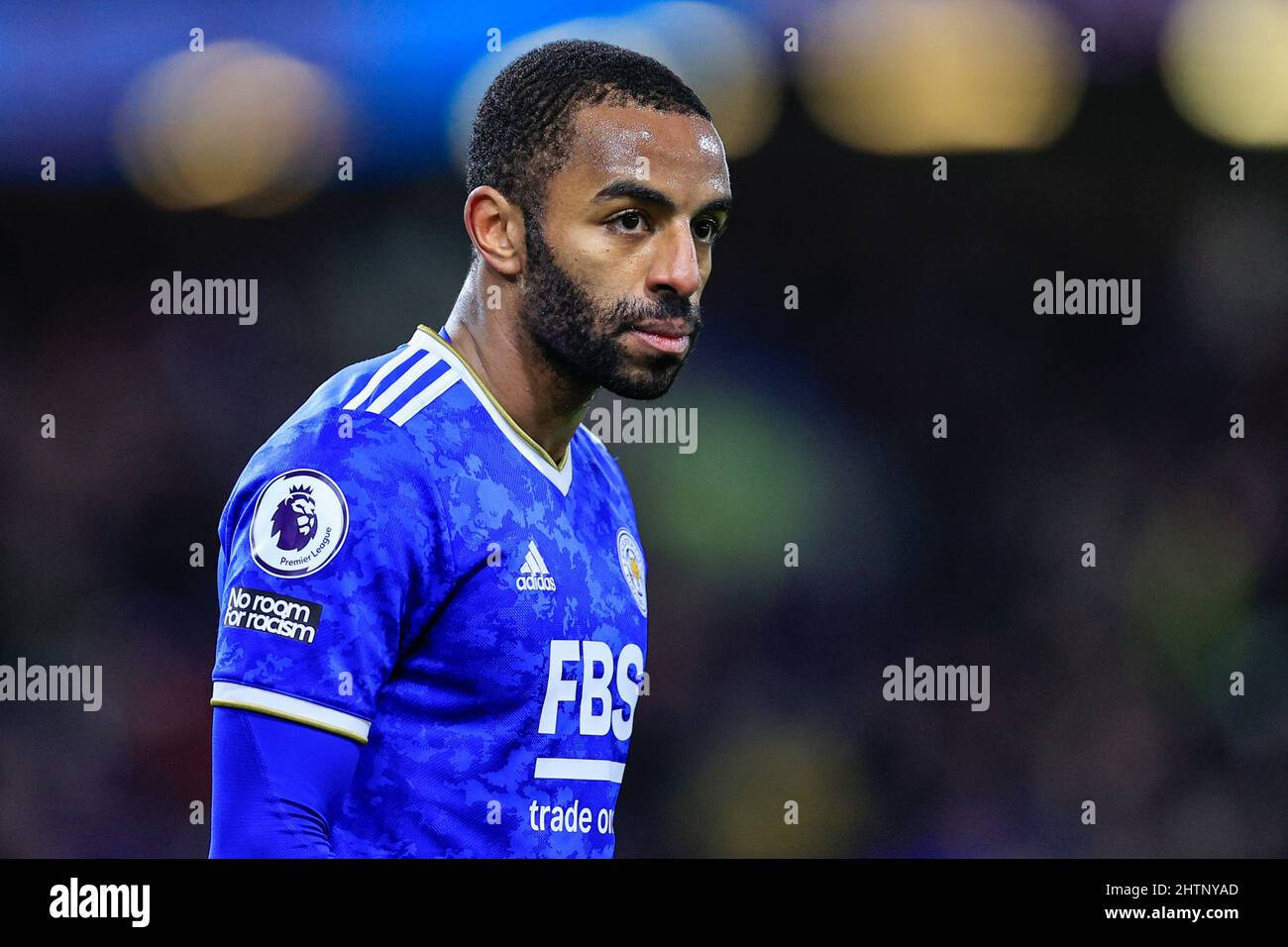 桌布 壁紙 — 一位專注的足球員身穿藍色萊斯特城球衣，站在模糊的球場上，在明亮的球場燈光下。