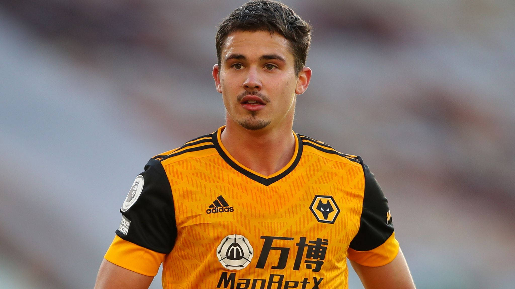 足球 桌布 壁紙 — 一位專注的足球員身穿黃黑狼隊球衣，站在陽光普照的球場上。