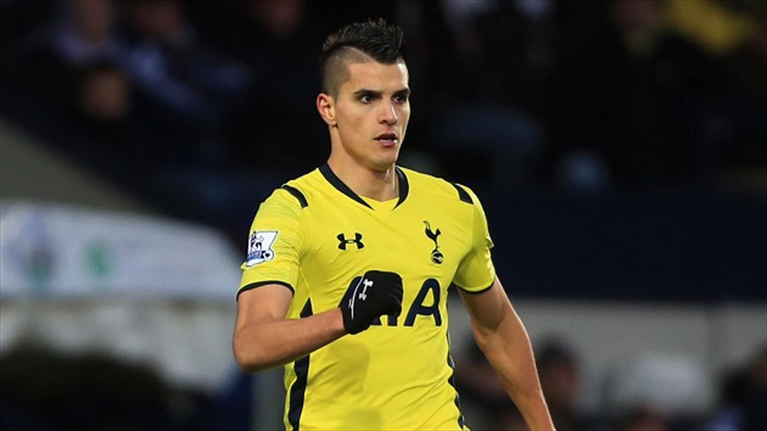 erik lamela 桌布 壁紙 — 一位專注的足球運動員穿著亮黃色的熱刺球衣，在夜間比賽中於球場燈光下奮力奔跑。