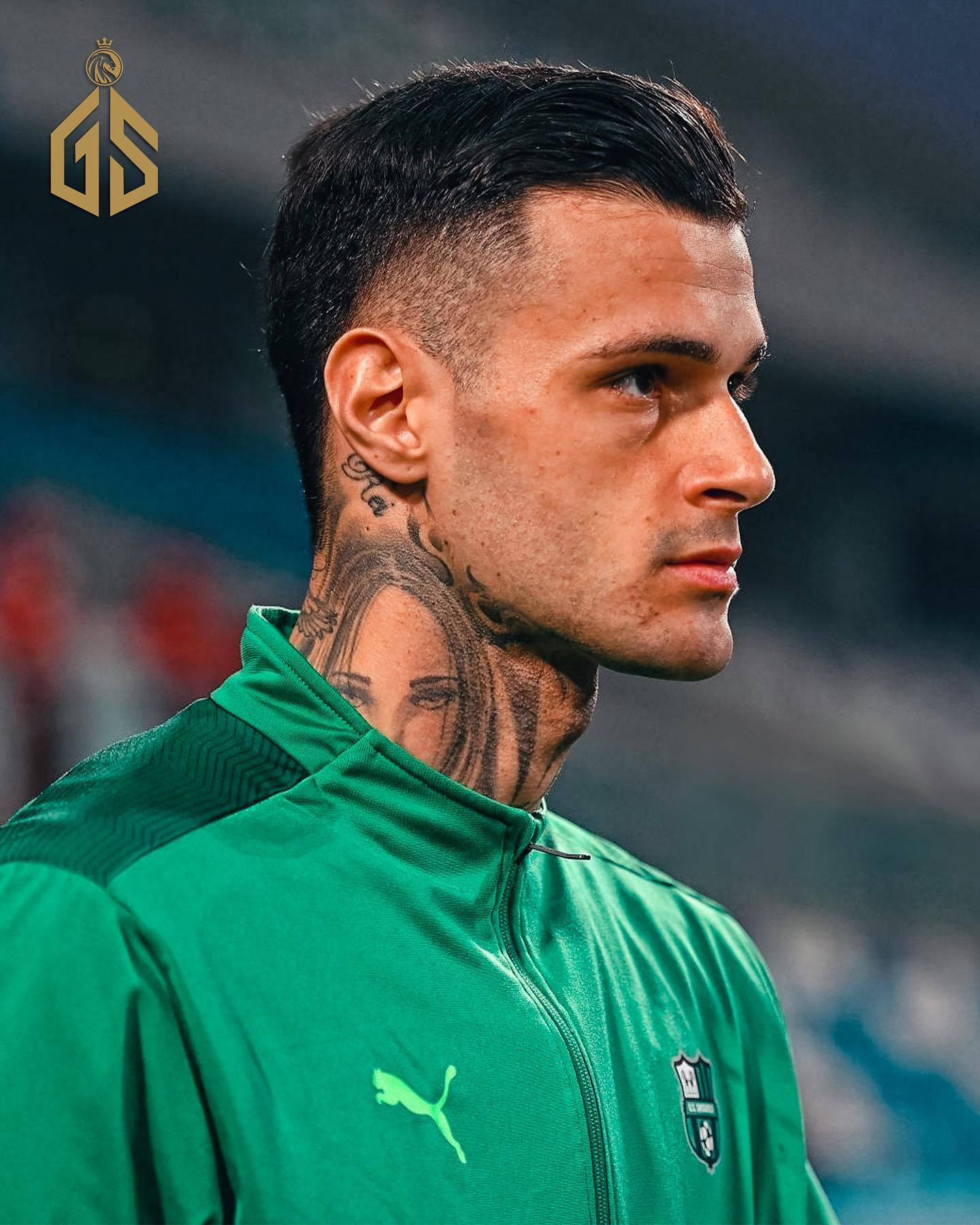 Athlete 桌布 壁紙 — 一位專注的足球運動員穿著綠色訓練外套，頸部有可見的紋身，在比賽中凝視著。