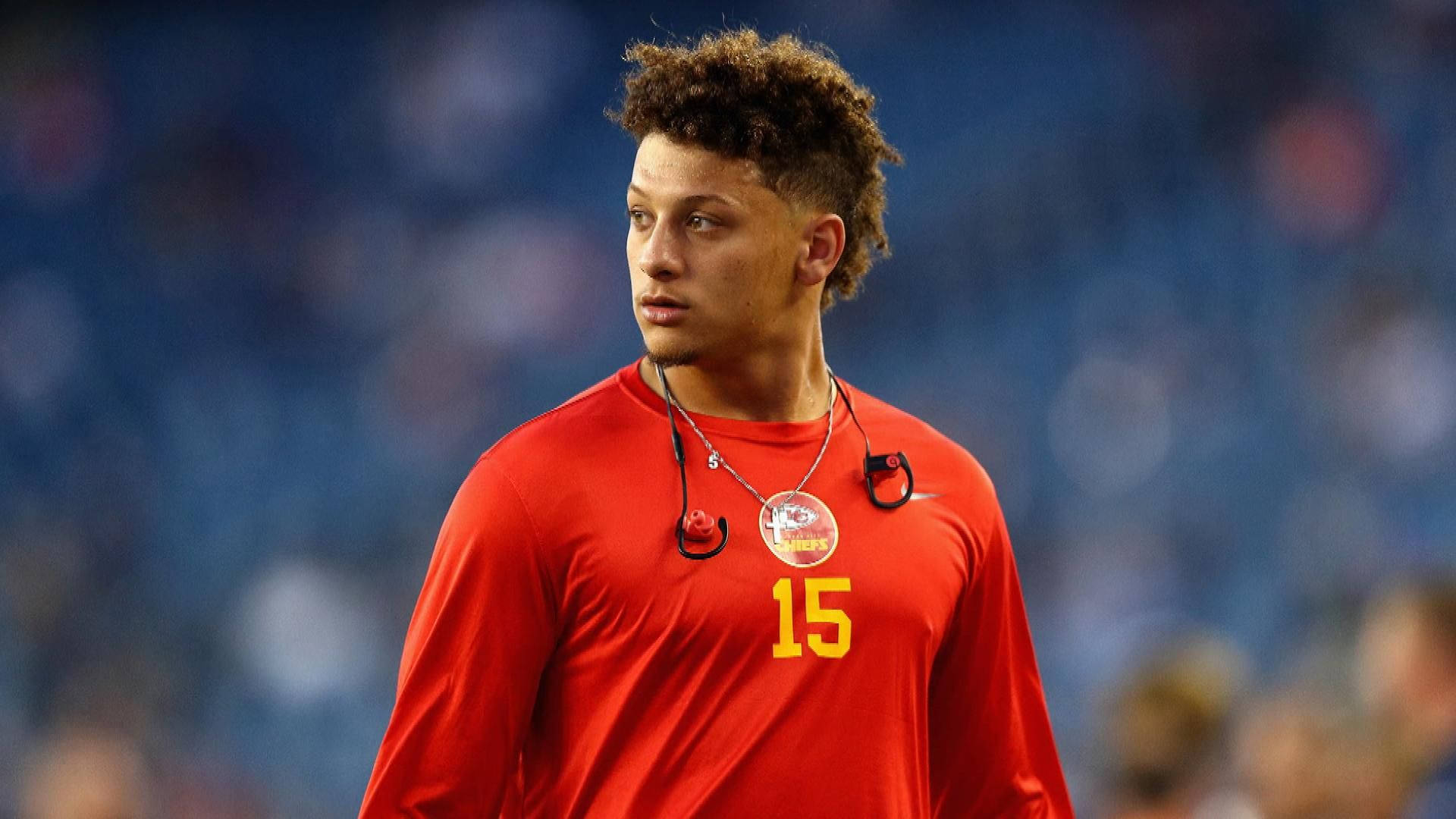 派翠克·馬霍姆斯 桌布 壁紙 — 一位專注的足球運動員身穿紅色球衣，號碼15，站在球場上，背景是模糊的體育場座位。