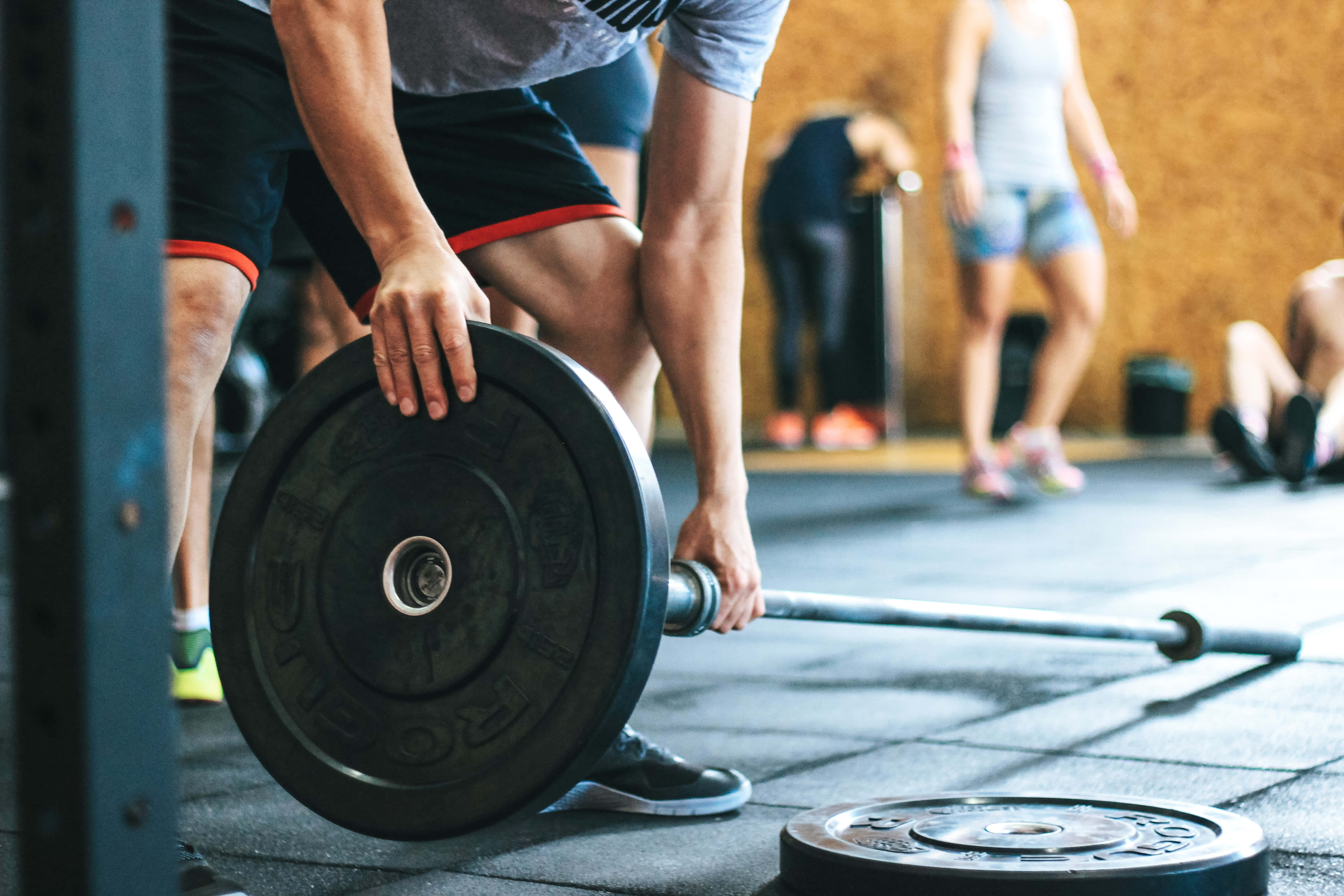 Barbell 桌布 壁紙 — 一位專注的運動員在健身房握著沉重的槓鈴，背景中有其他人在訓練。