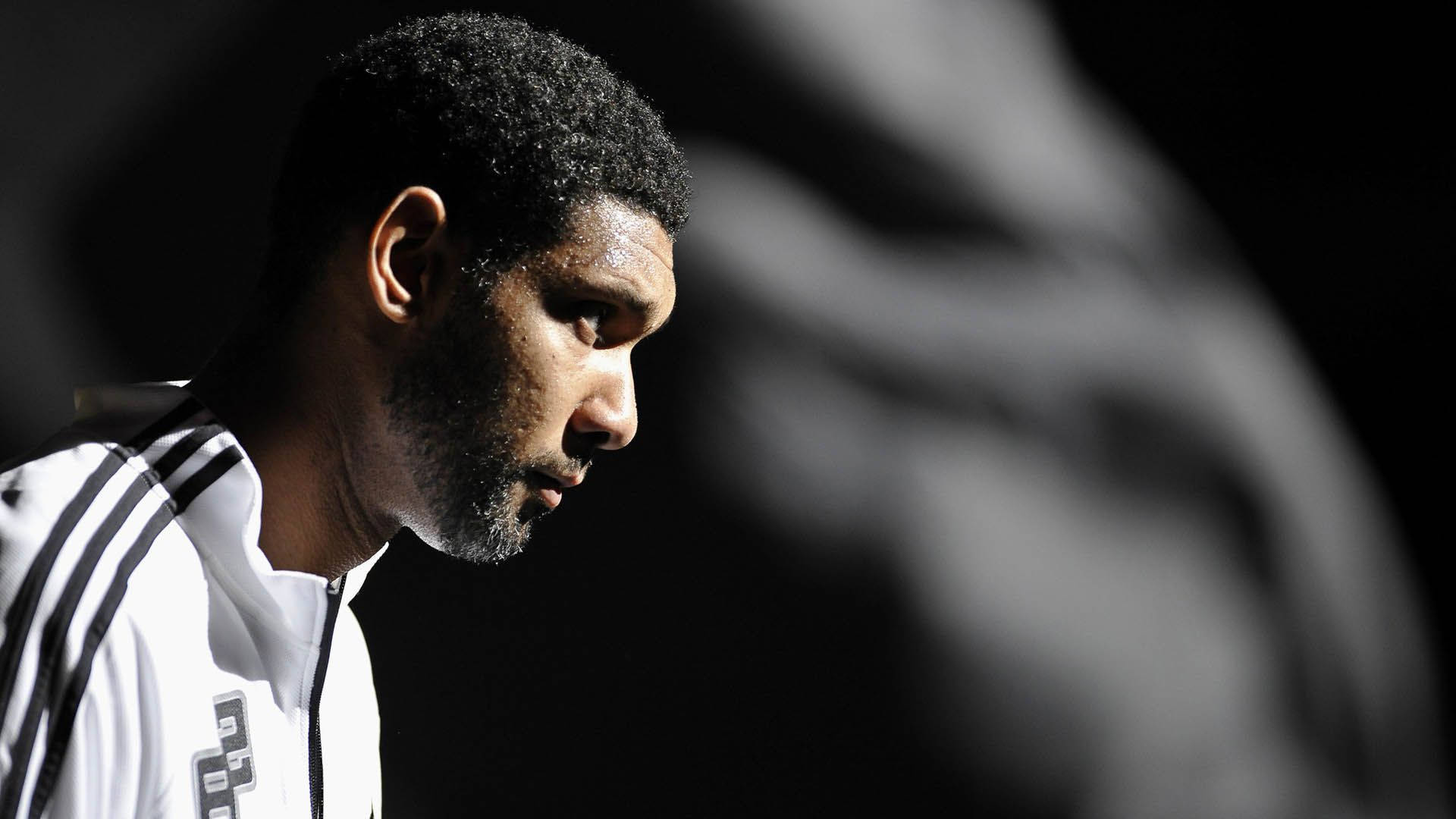 Tim Duncan 桌布 壁紙 — 一位專注的運動員穿著白色運動外套，在模糊的深色背景下向下凝視。