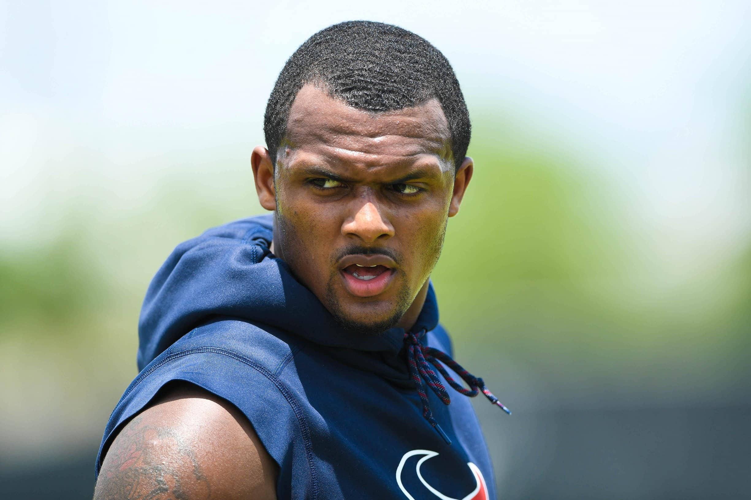 Deshaun Watson 桌布 壁紙 — 一位專注的運動員穿著藍色無袖連帽衫，在明亮的日光下進行戶外訓練時，眼神銳利。