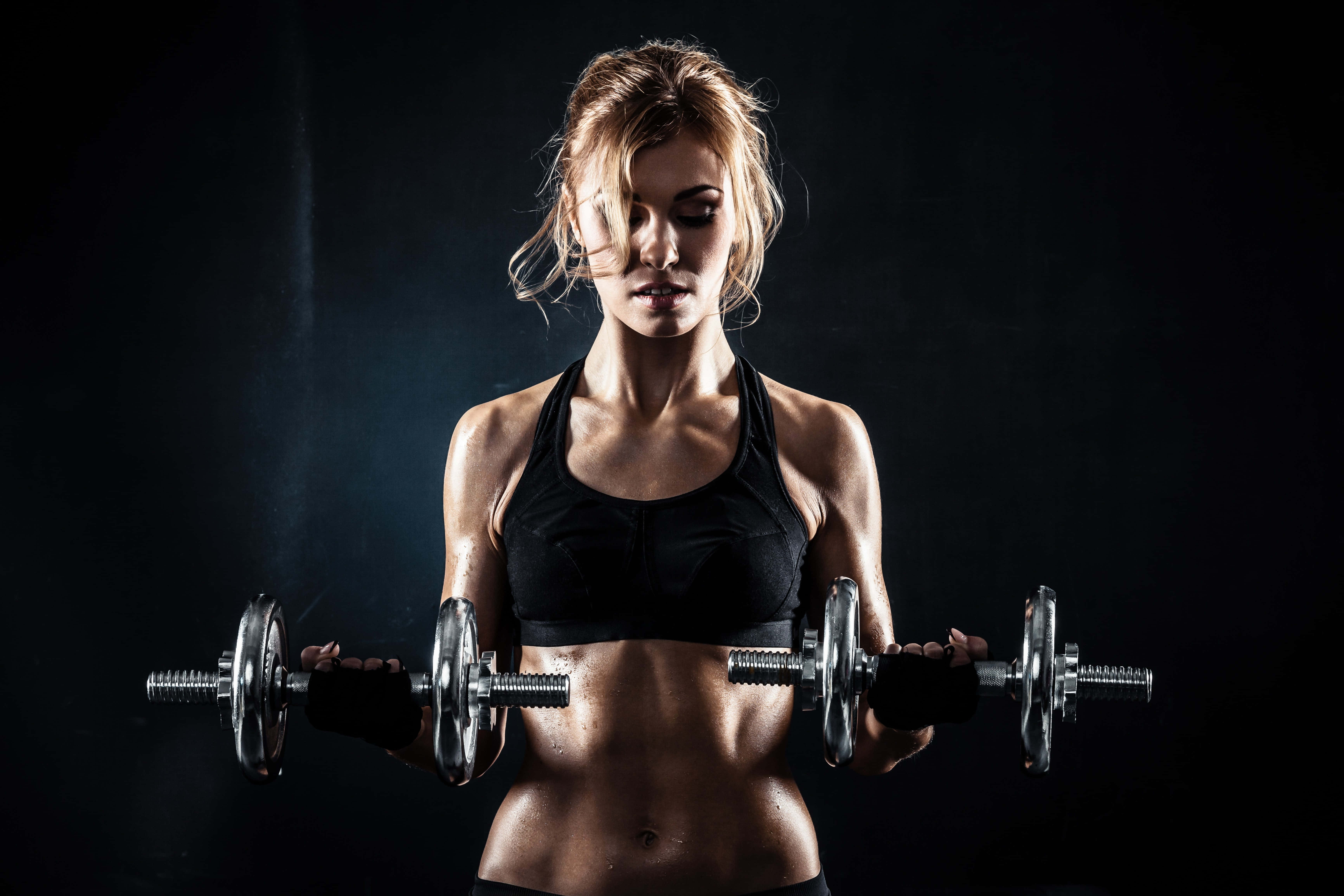 Athletic 桌布 壁紙 — 一位專注的運動女性，擁有明顯的腹肌，在昏暗的攝影棚背景下，配合戲劇性的燈光，手持啞鈴。