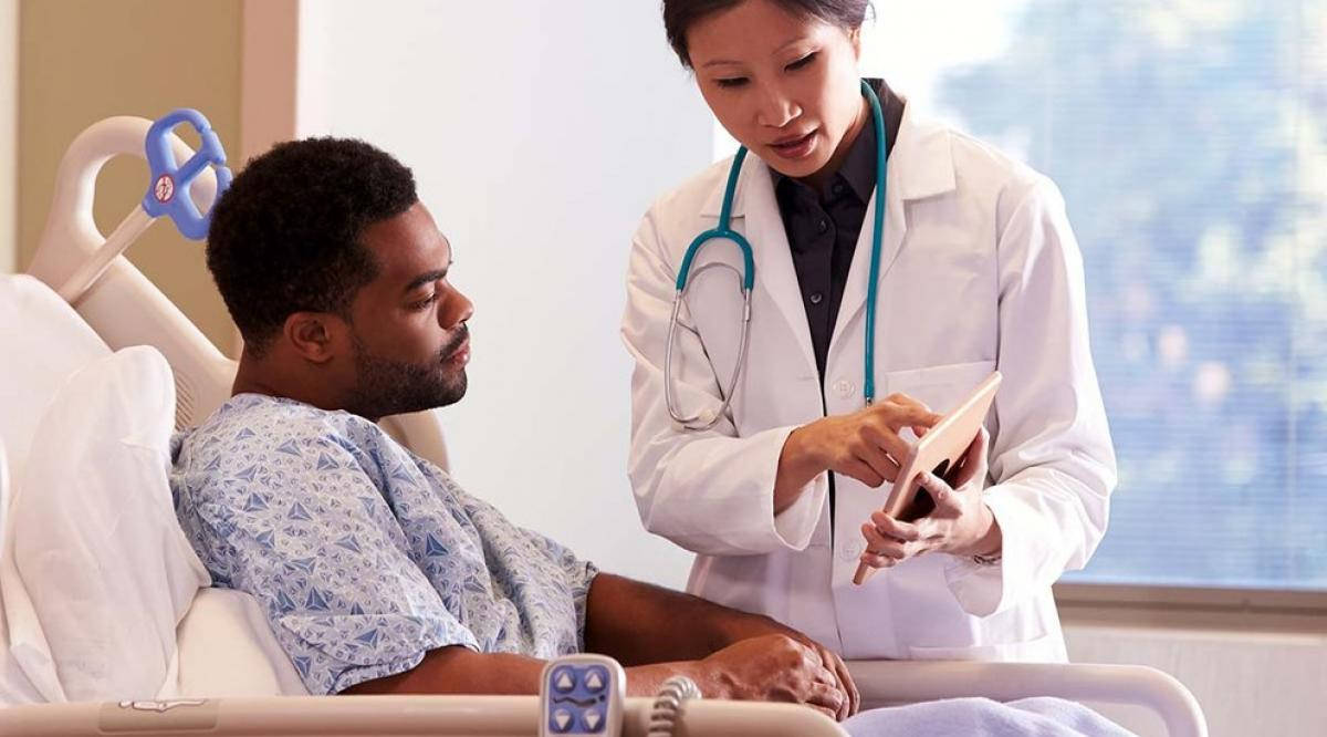 Stethoscope 桌布 壁紙 — 一位專注的醫生穿著白袍，在醫院病床邊照顧病人時使用平板電腦。