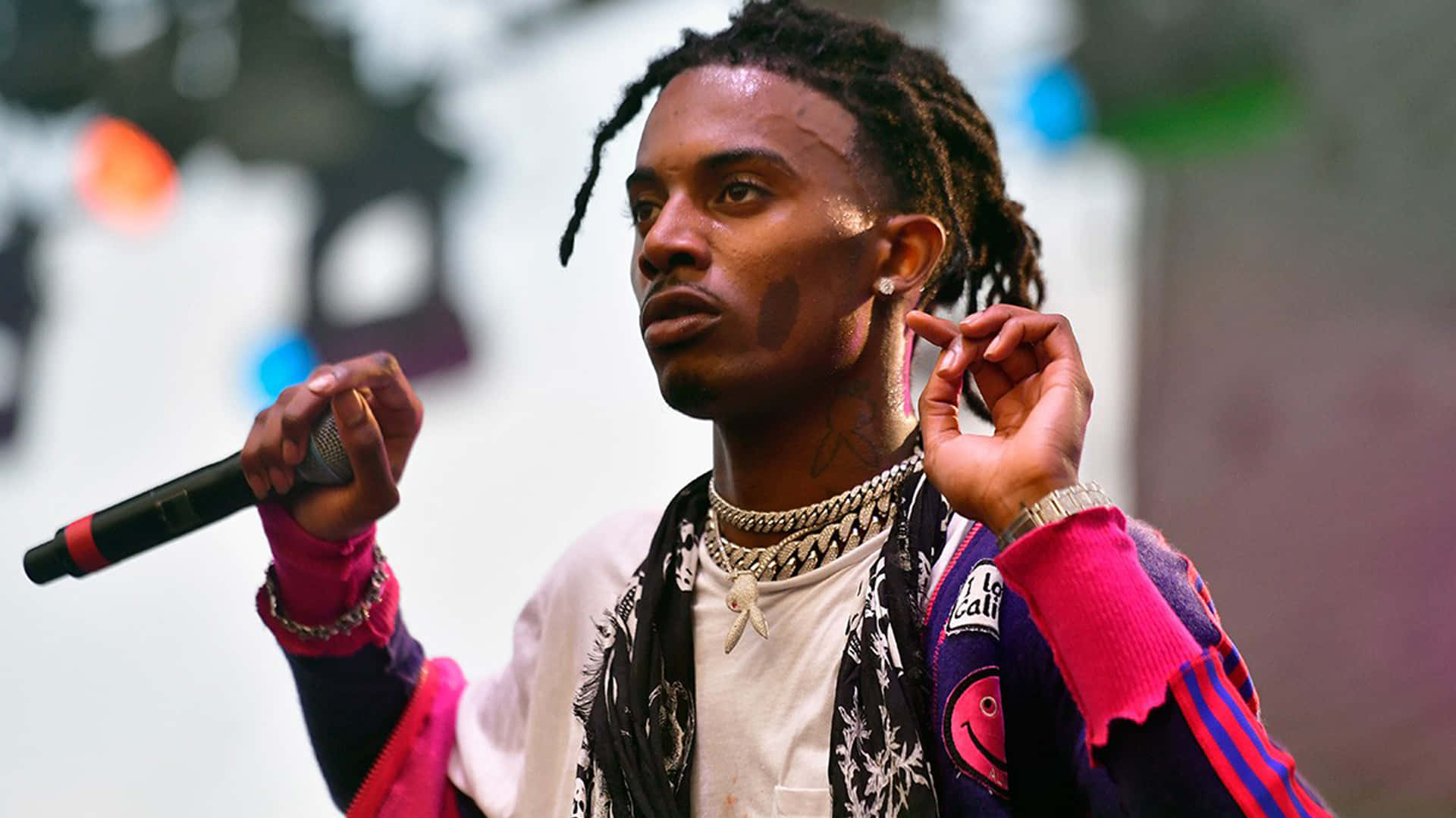 Playboi Carti HD 桌布 壁紙 — 一位專注的雷鬼辮說唱歌手在燈光明亮的舞台上拿著麥克風調整耳機。
