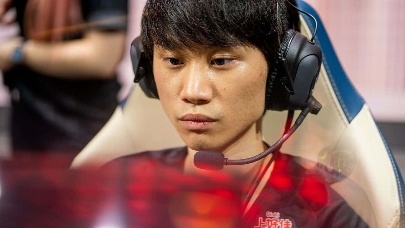 Esports 桌布 壁紙 — 一位專注的電競選手，深色頭髮，戴著黑色耳機，身穿紅色發光球衣，坐在電競椅上。