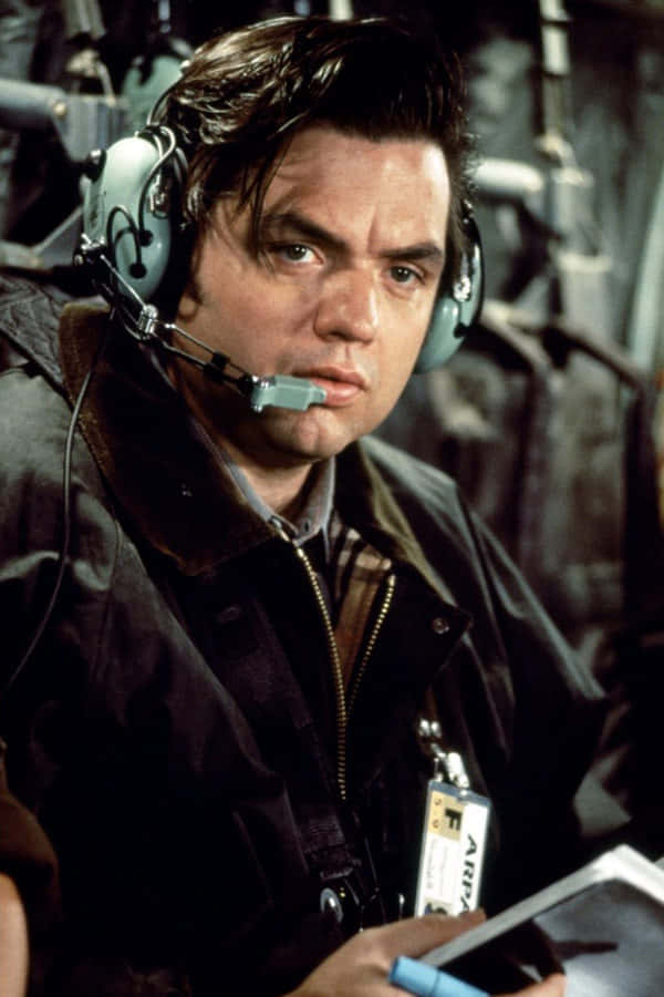 Oliver Platt 桌布 壁紙 — 一位專注的飛行員在駕駛艙內戴著耳機，手持剪貼板，表情嚴肅。