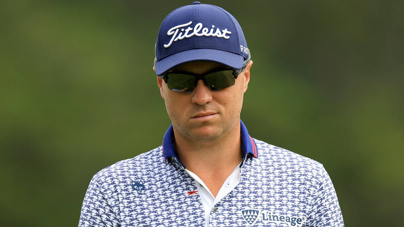 高爾夫 桌布 壁紙 — 一位專注的高爾夫球手，戴著藍色 Titleist 帽子和圖案 Polo 衫，站在模糊的綠色背景前。