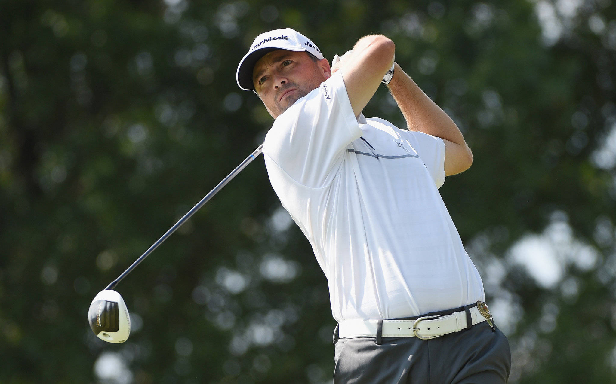 Ryan Palmer 桌布 壁紙 — 一位專注的高爾夫球手在明亮的日光下，以模糊的綠色樹木為背景揮桿。