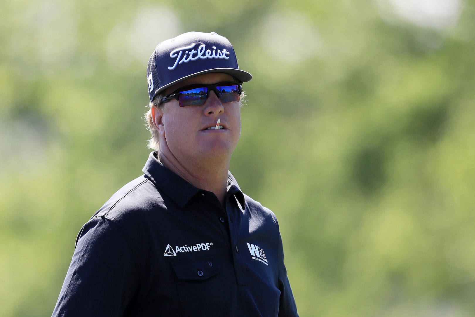 高爾夫 桌布 壁紙 — 一位專注的高爾夫球手戴著海軍藍 Titleist 帽和太陽眼鏡，站在模糊的綠色背景前。