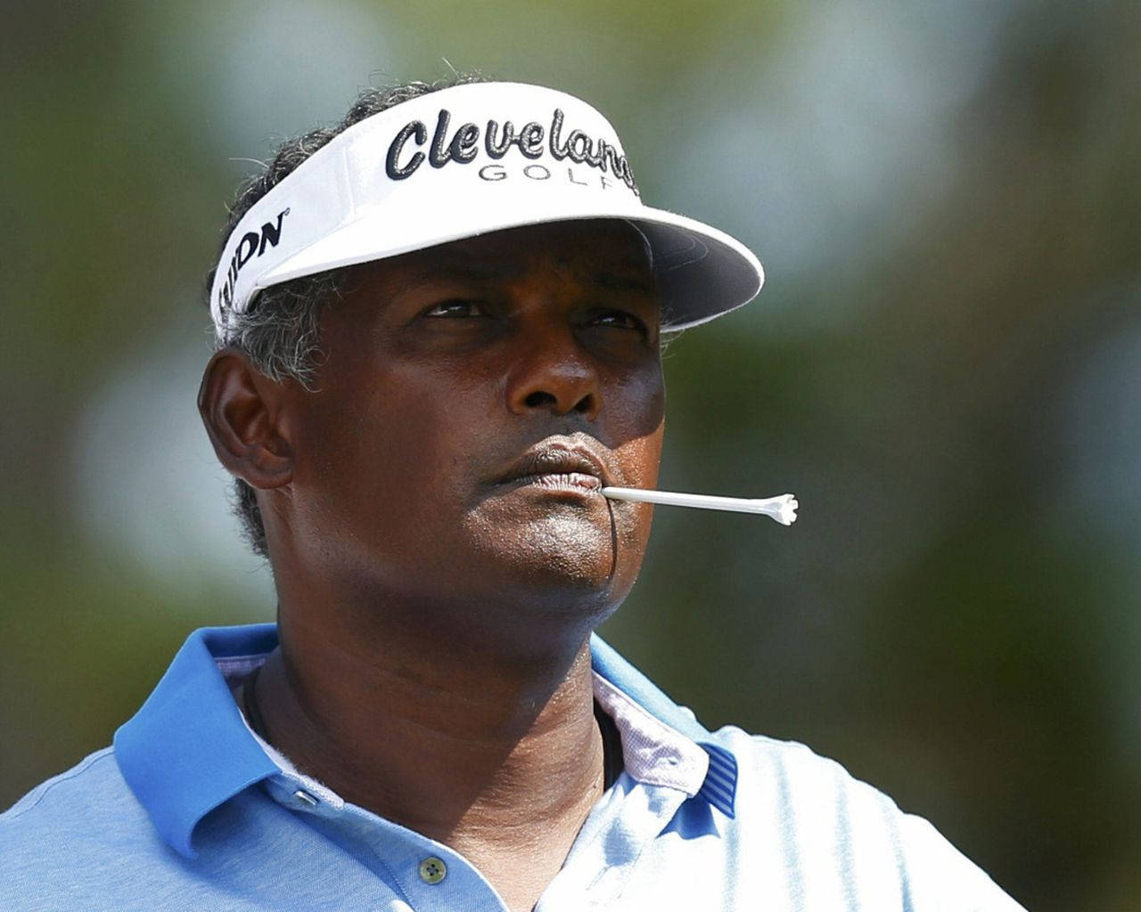 高爾夫 桌布 壁紙 — 一位專注的高爾夫球手戴著白色 Cleveland Golf 遮陽帽，嘴裡叼著高爾夫球座，背景是模糊的綠色。