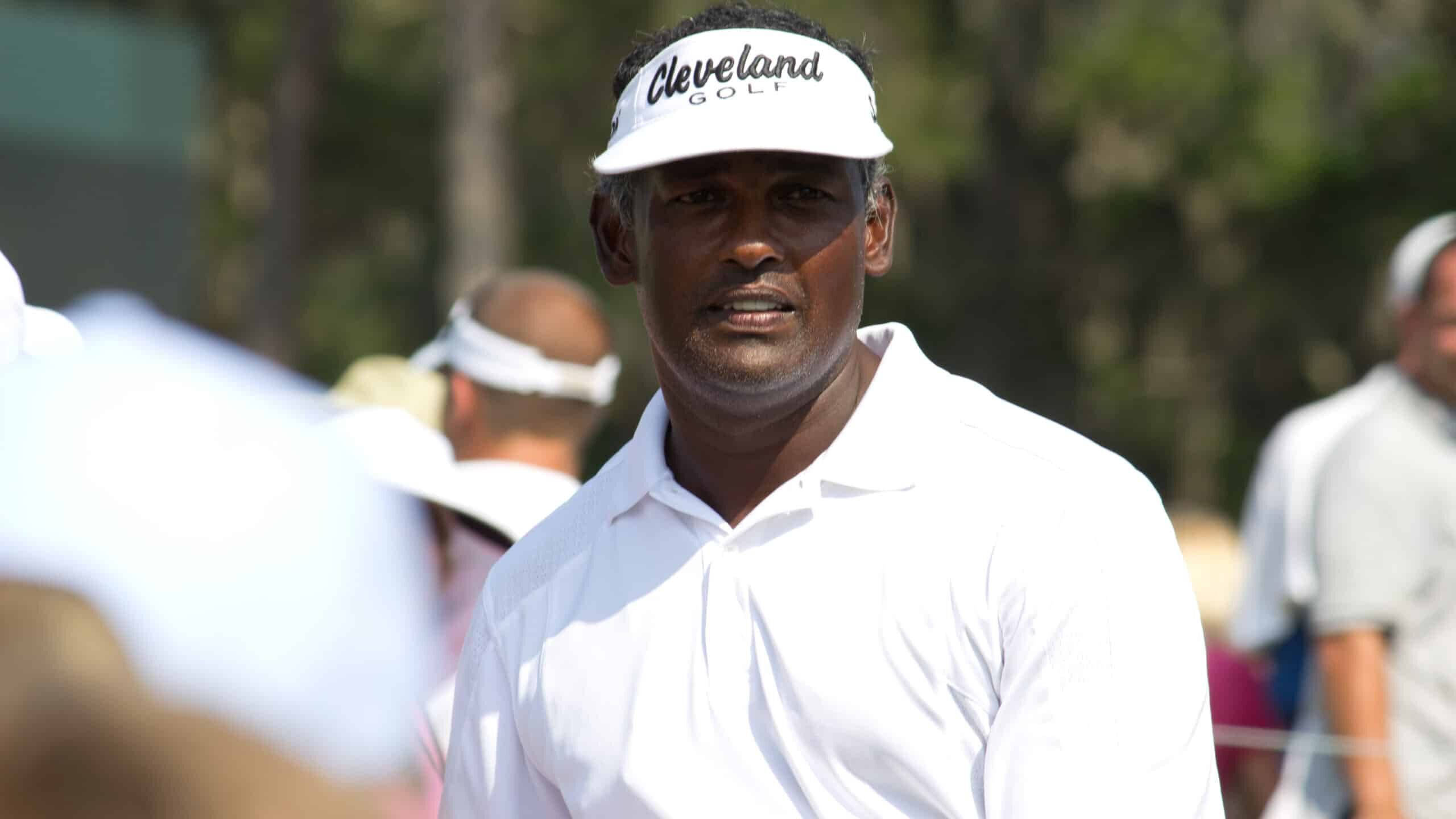 高爾夫 桌布 壁紙 — 一位專注的高爾夫球手戴著白色 Cleveland Golf 遮陽帽和 Polo 衫，站在陽光明媚的球場上，背景有模糊的觀眾和樹木。