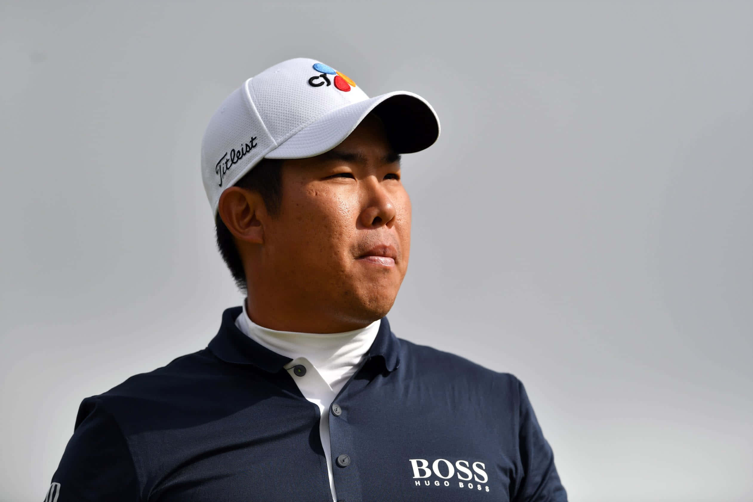 Man 桌布 壁紙 — 一位專注的高爾夫球手戴著白色帽子，身穿海軍藍 Hugo Boss 馬球衫，站在純灰色背景前。