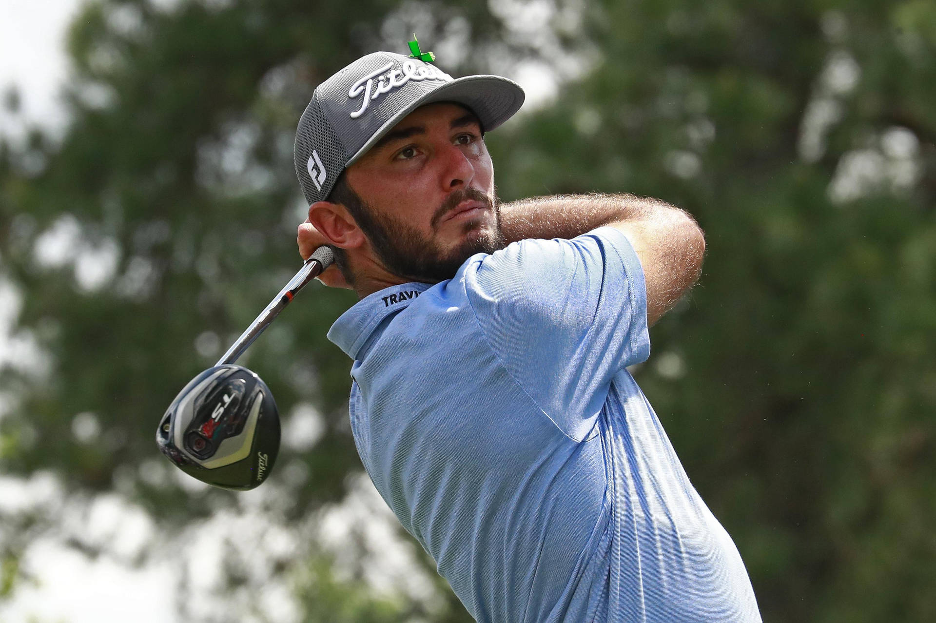  壁紙 — 一位專注的高爾夫球手正在揮桿，使用 Titleist 一號木桿，背景是模糊的綠色樹木。