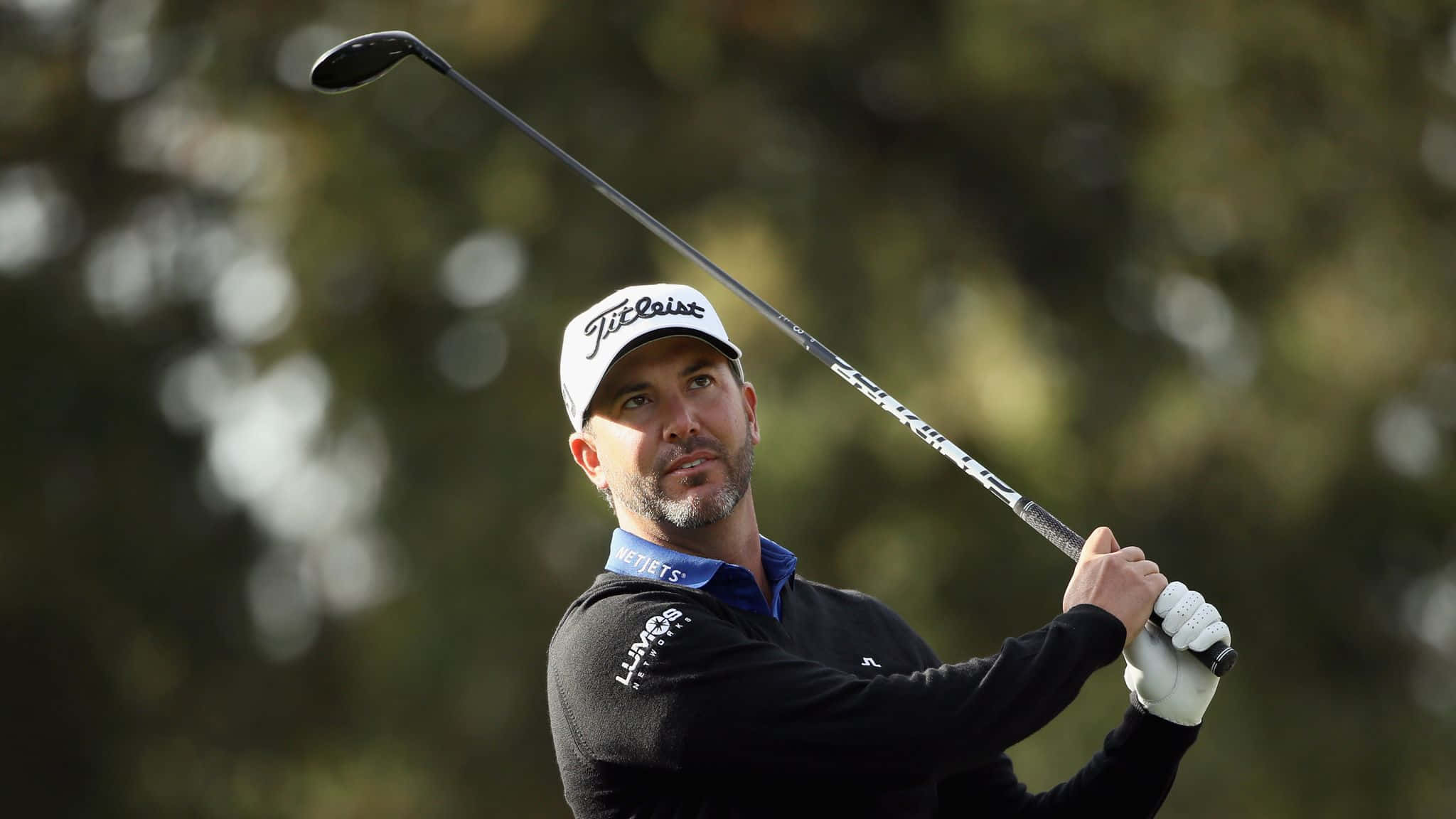高爾夫 桌布 壁紙 — 一位專注的高爾夫球手正在揮桿，使用 Titleist 一號木桿，背景是模糊的綠色樹木。