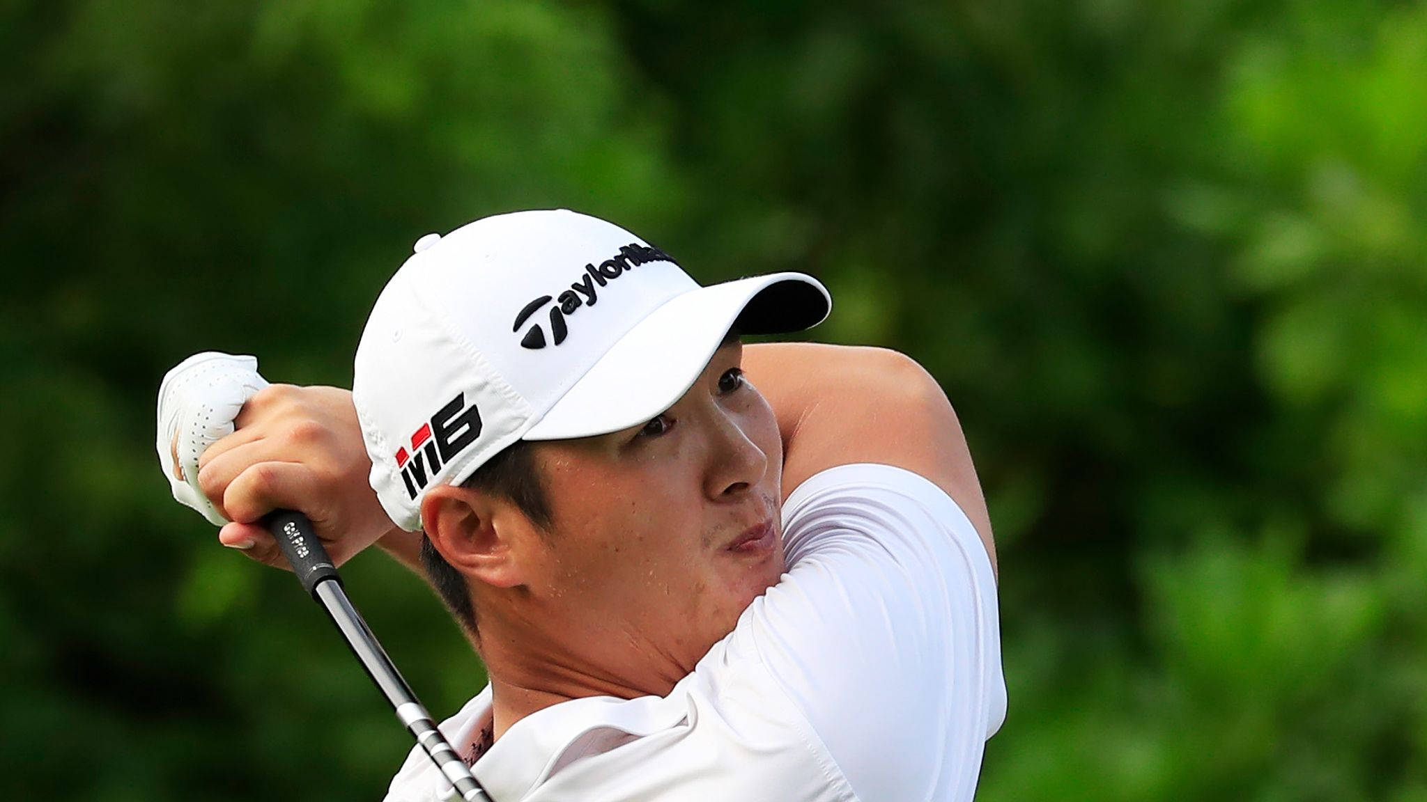 Athlete 桌布 壁紙 — 一位專注的高爾夫球手正在揮桿，戴著白色帽子和襯衫，背景是模糊的綠色。