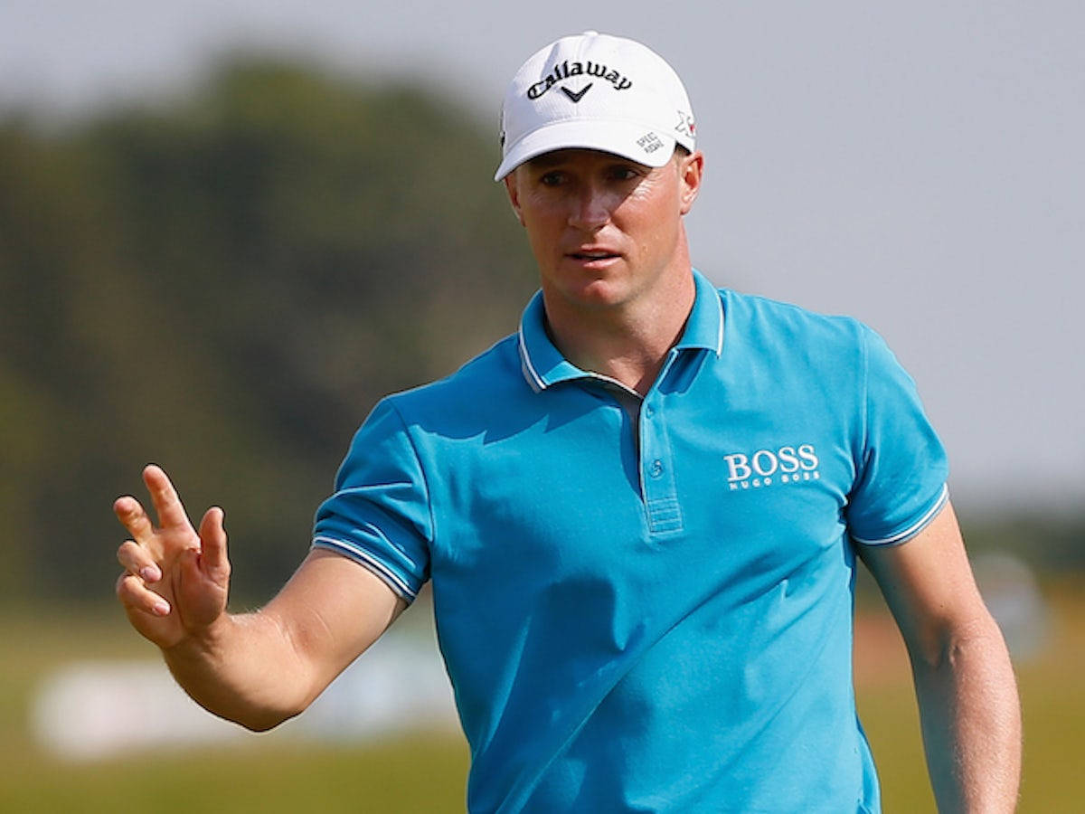運動 桌布 壁紙 — 一位專注的高爾夫球手穿著藍色 Hugo Boss 馬球衫和白色 Callaway 帽子，在陽光明媚的球場上揮桿時做手勢。